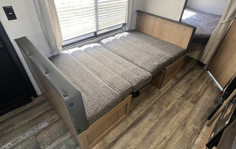 Cozy RV rental interior showcasing a convertible dinette bed, window with blinds, and wood-look flooring. Ready for travel.. Forest River 26' Bunkhouse 2025