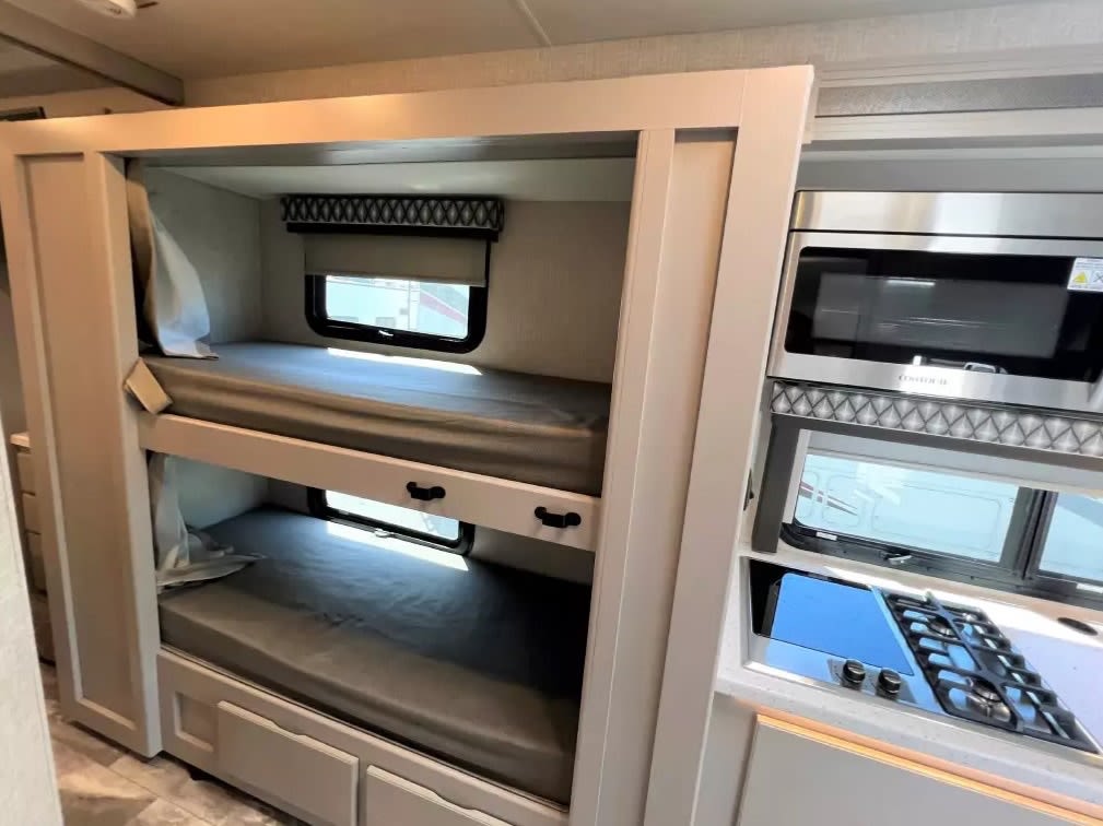 Cozy bunk beds with windows and a compact kitchen in this RV rental, offering comfortable RV interior living.. Thor Motor Coach Quantum LF31 2023