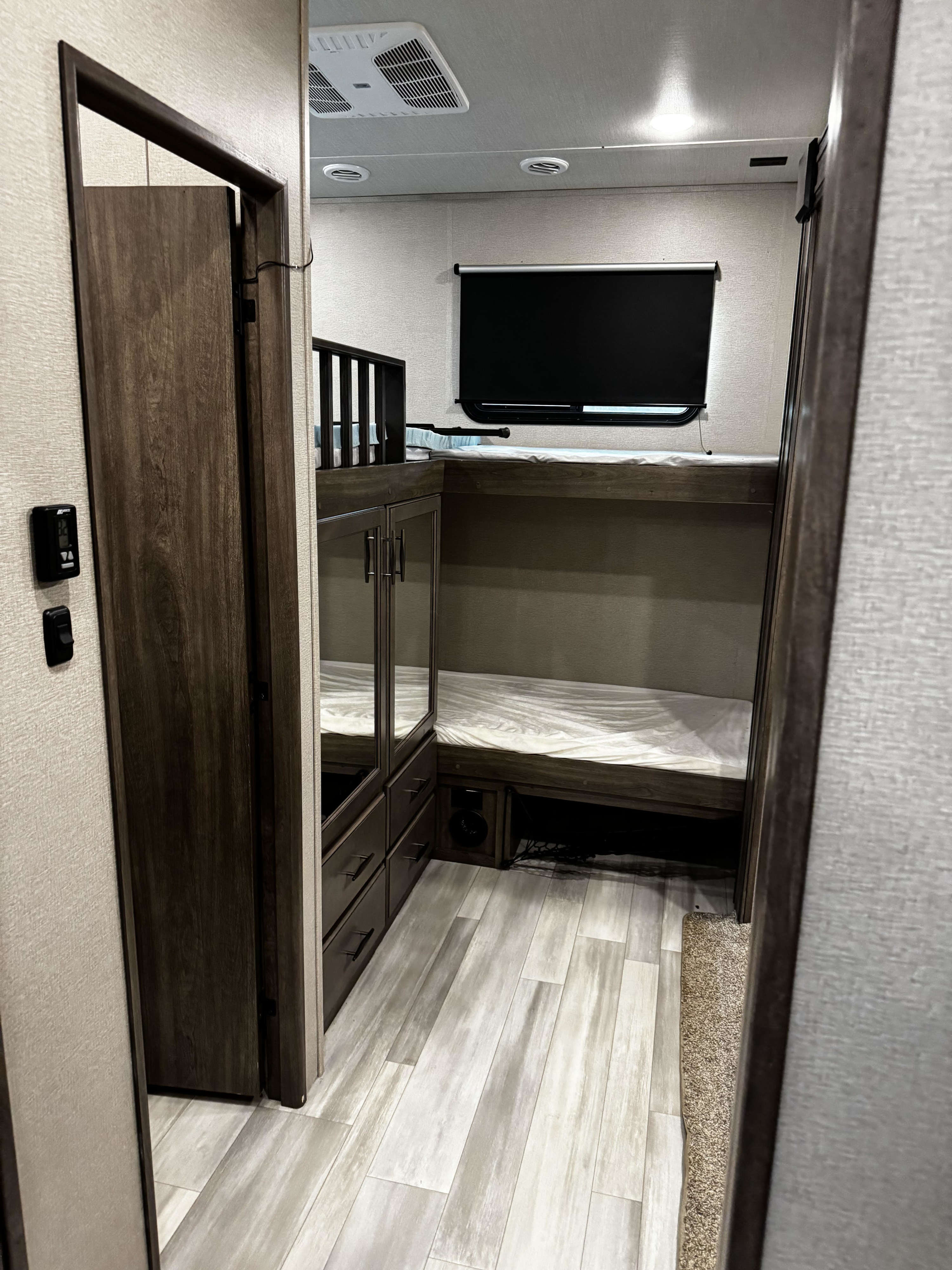 RV rental bunkhouse features a cozy bedroom with stacked beds, TV, wardrobe, and storage. Perfect for family adventures.. Grand Design Solitude 2023