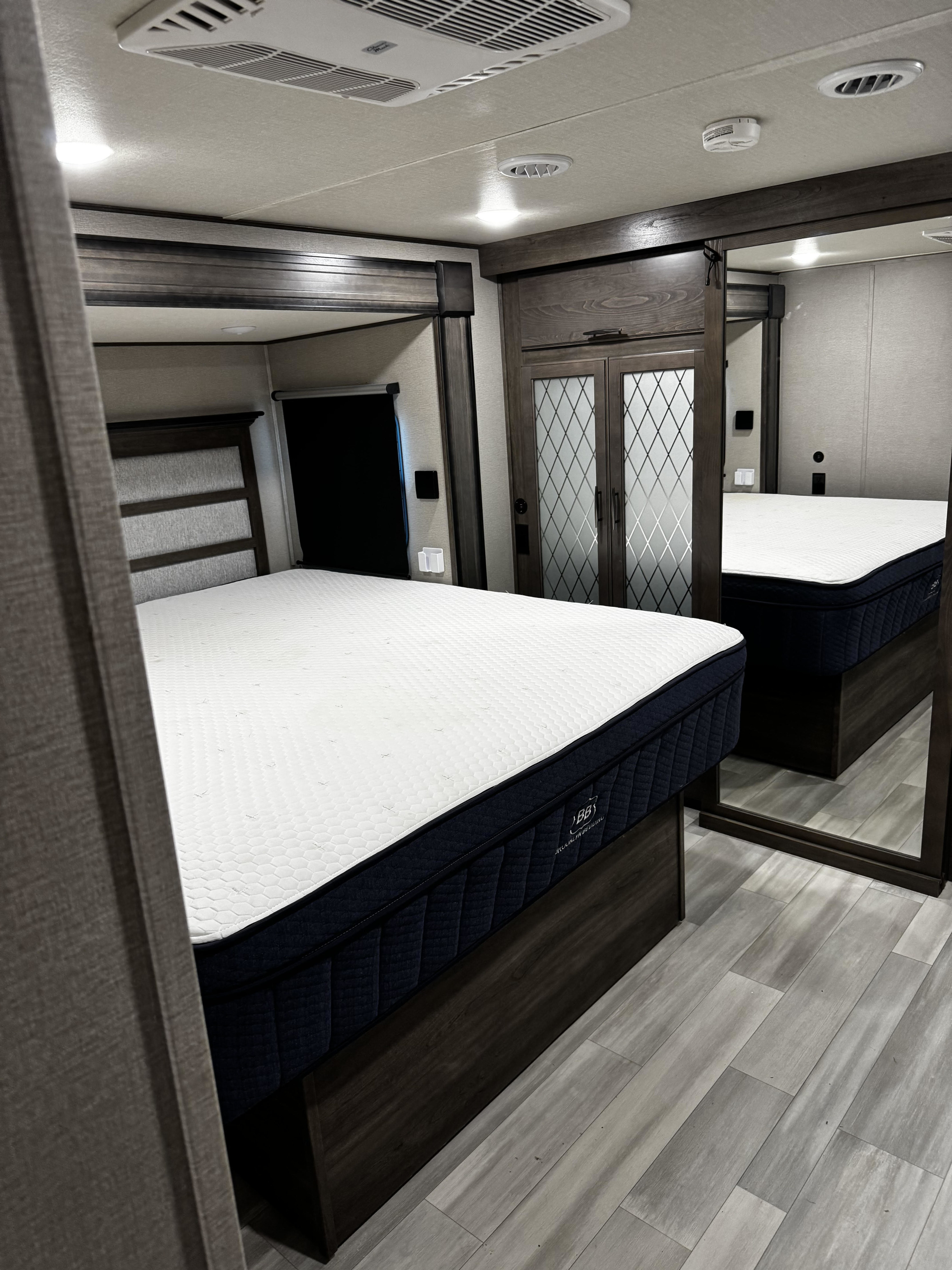 RV rental bedroom showcasing a plush queen bed, mirrored wardrobe, modern wood accents, and light flooring.. Grand Design Solitude 2023