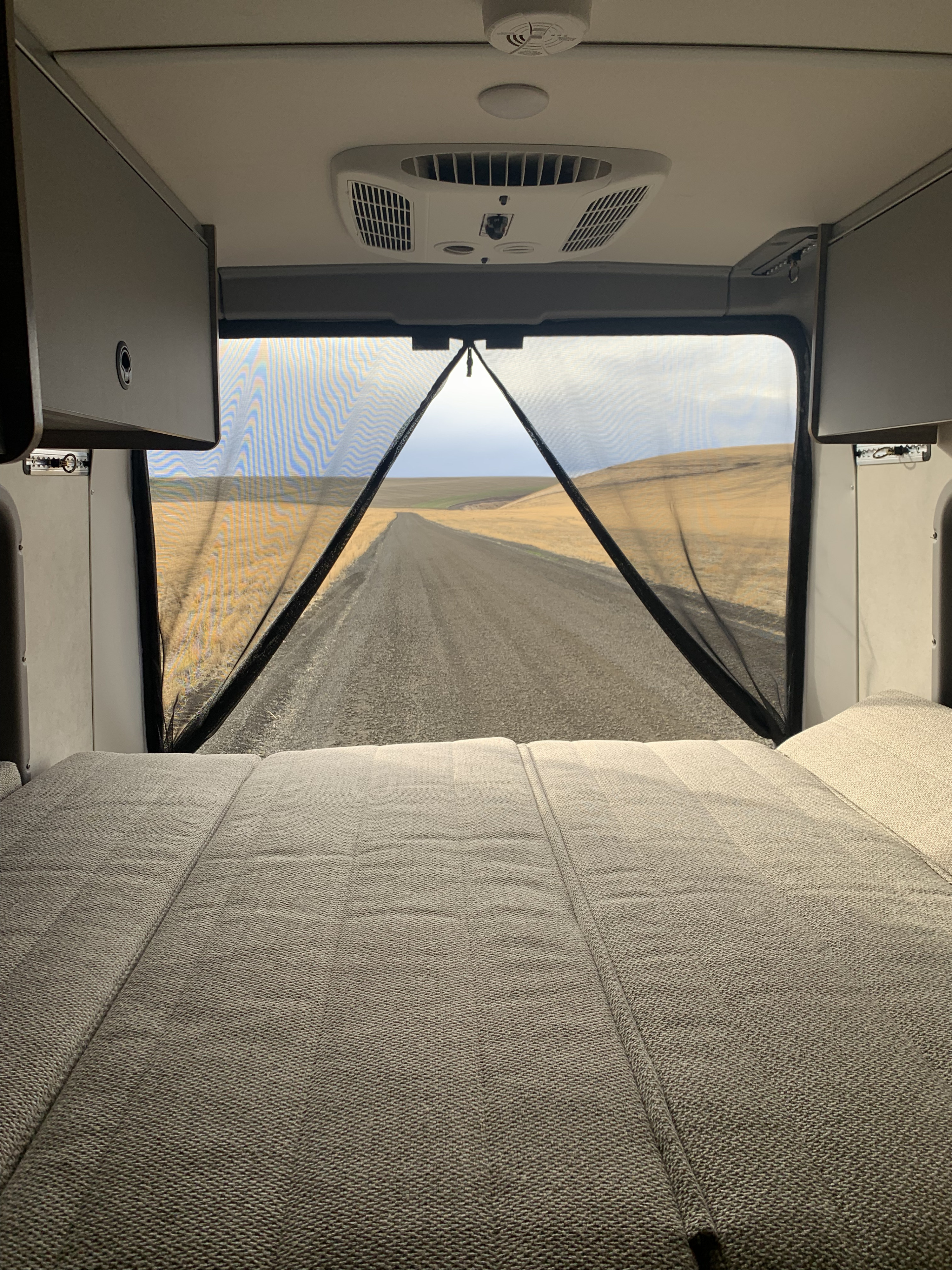 View from an rv rental: comfy bed, bug screen, & a long road winding through endless fields.. Winnebago Solis 59PX 2025