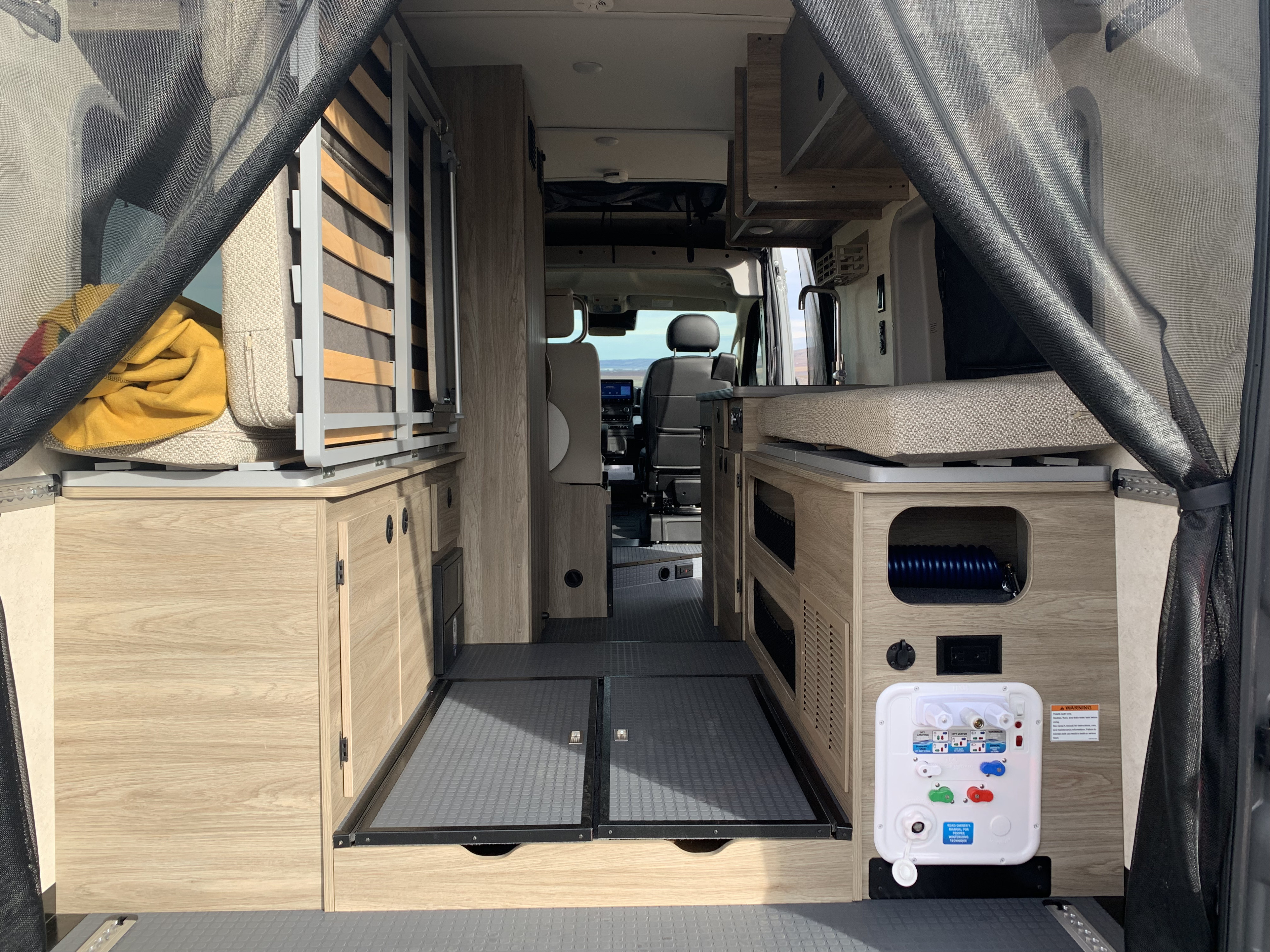 Inside an RV rental: rear view of the living area with light wood cabinetry, flexible bed/seating, and utility panel.. Winnebago Solis 59PX 2025