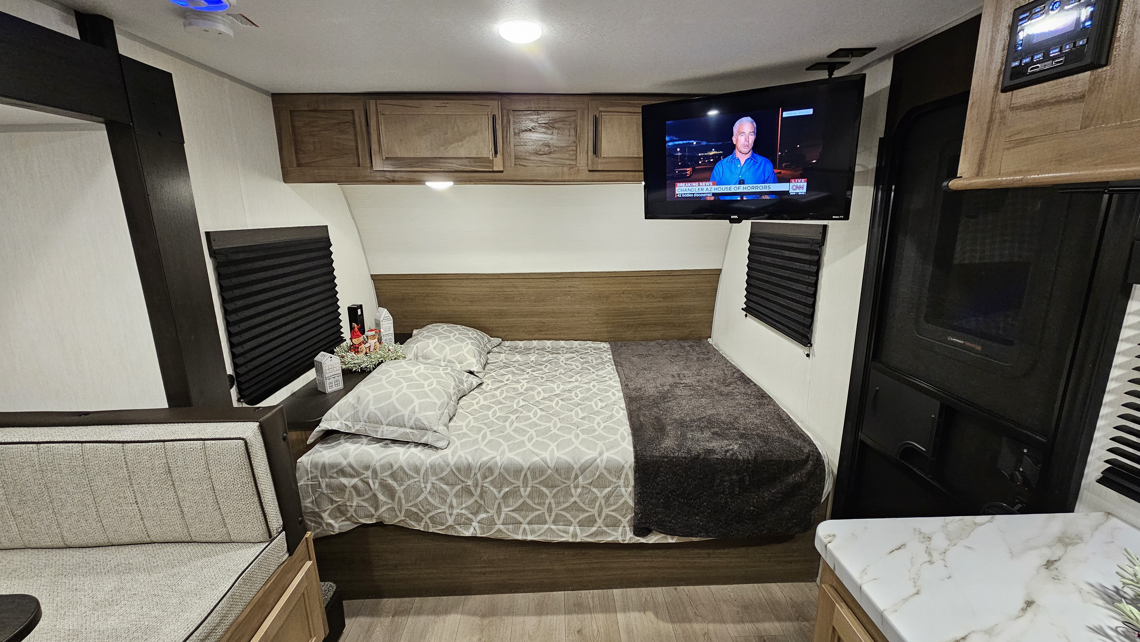 Relax in this RV rental's cozy bedroom: patterned bed, wall-mounted TV, overhead cabinets, and adjacent seating.. Forest River 17JW 2025