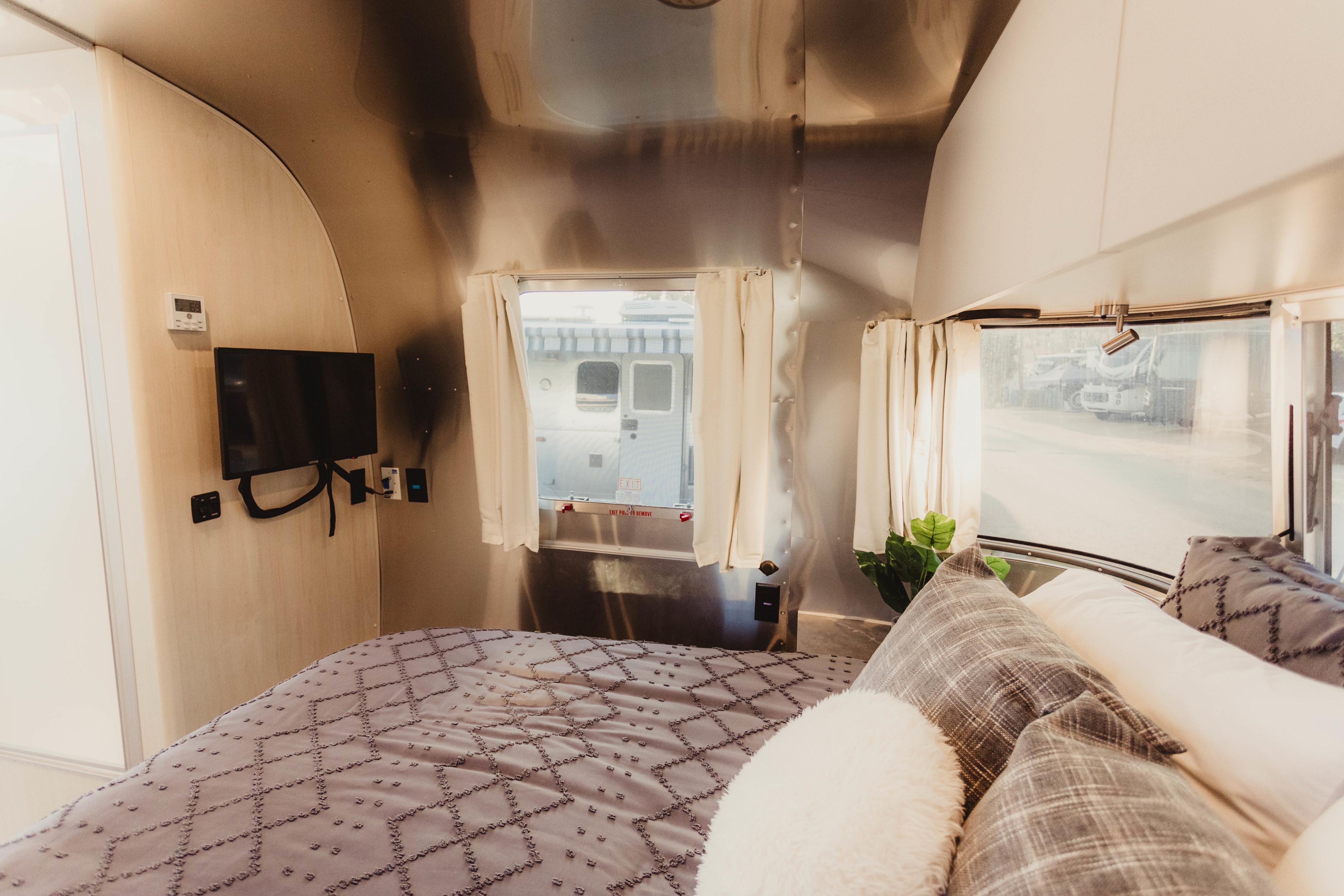 Stylish RV rental interior with a cozy bed, plaid pillows, TV, and iconic aluminum walls.. Airstream Flying Cloud 2024