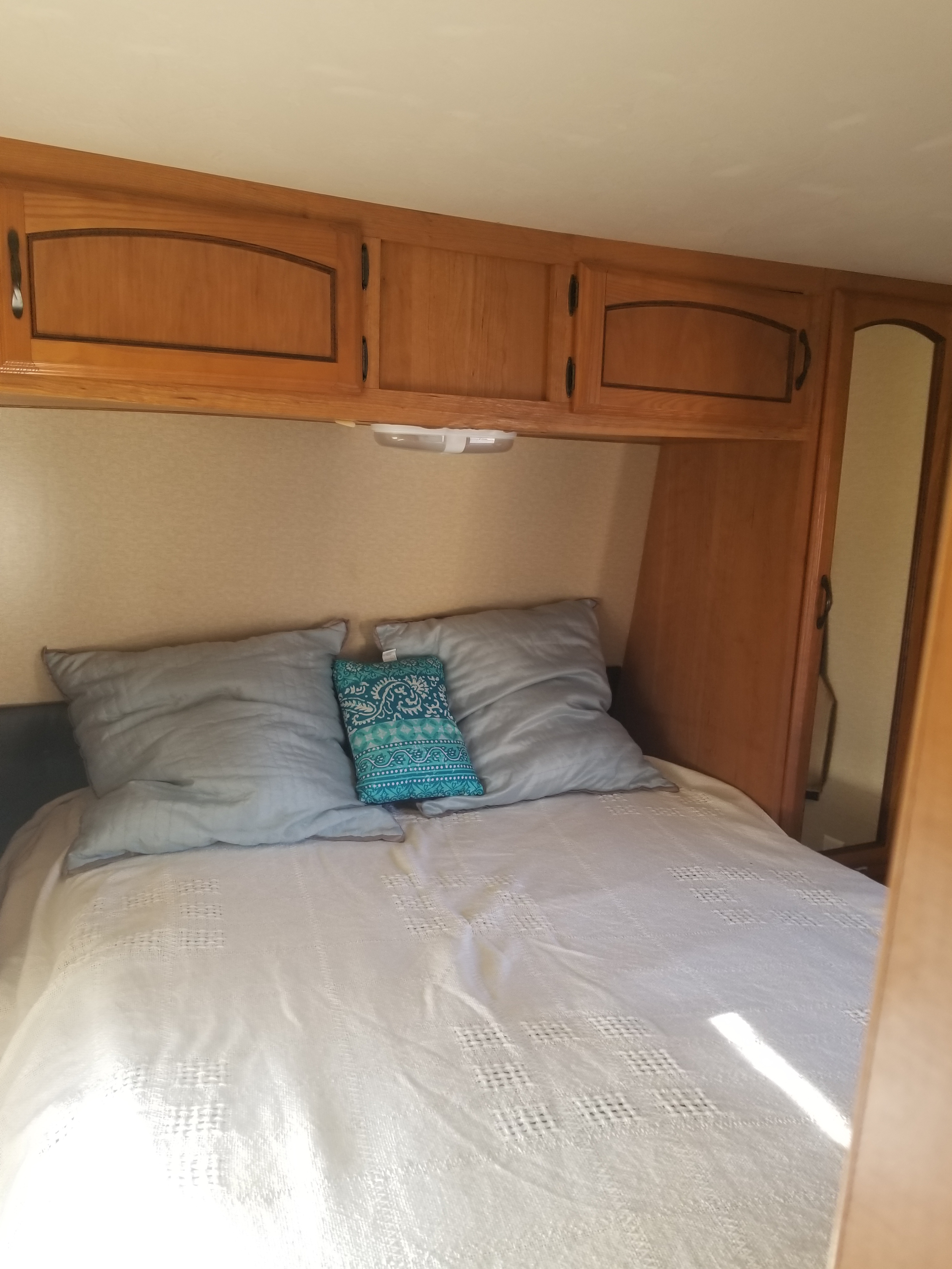 Inside an RV rental: a bright bedroom with wooden cabinets, a comfortable bed, and natural light streaming in.. Forest River Salem 2012
