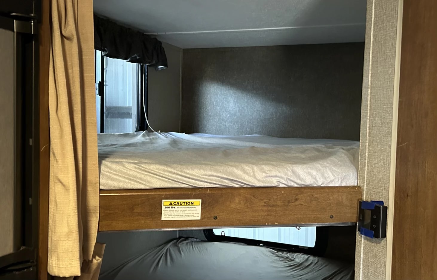 Bunk beds inside an RV rental. The upper bed has a 300 lbs weight limit, with curtains to the left and a wall control panel.. Keystone RV Springdale 2018