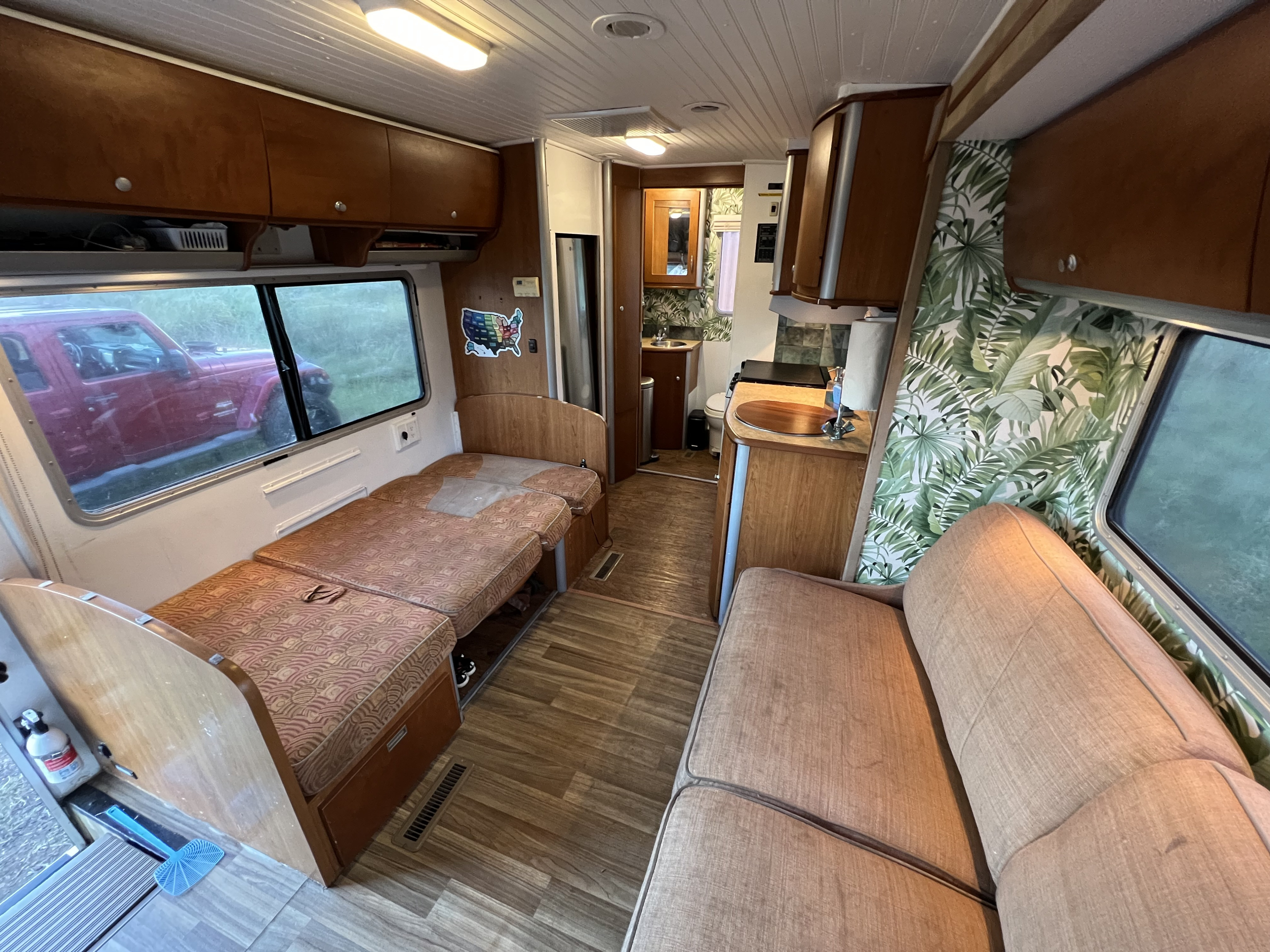 Bright rv rental interior featuring a versatile living/sleeping area, well-equipped kitchenette, and accessible bathroom. Palm print accents add flair.. Winnebago View 2005