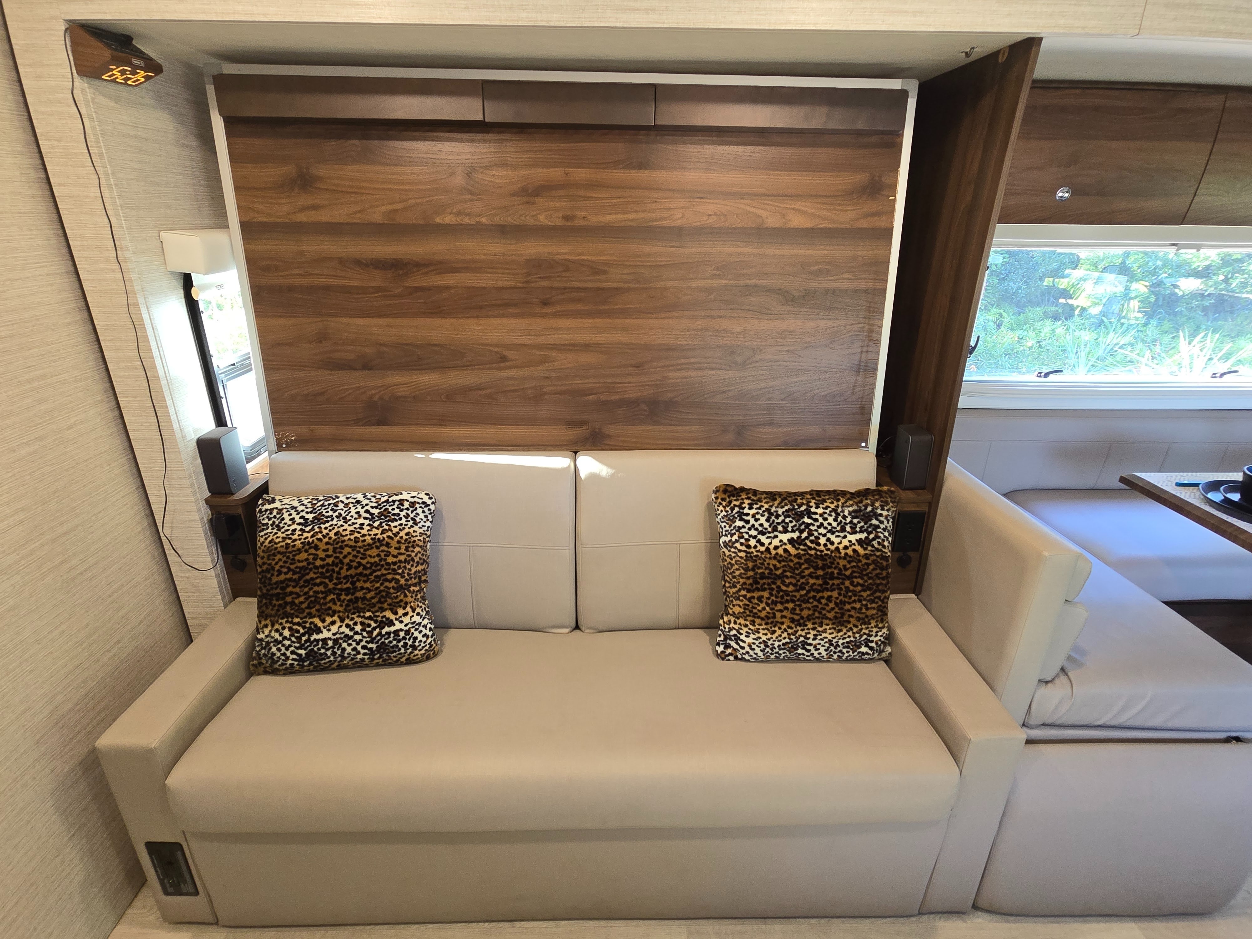 Compact RV rental interior with a light-colored sofa, leopard print pillows, a wooden fold-down bed, and a dinette.. Winnebago View 2022