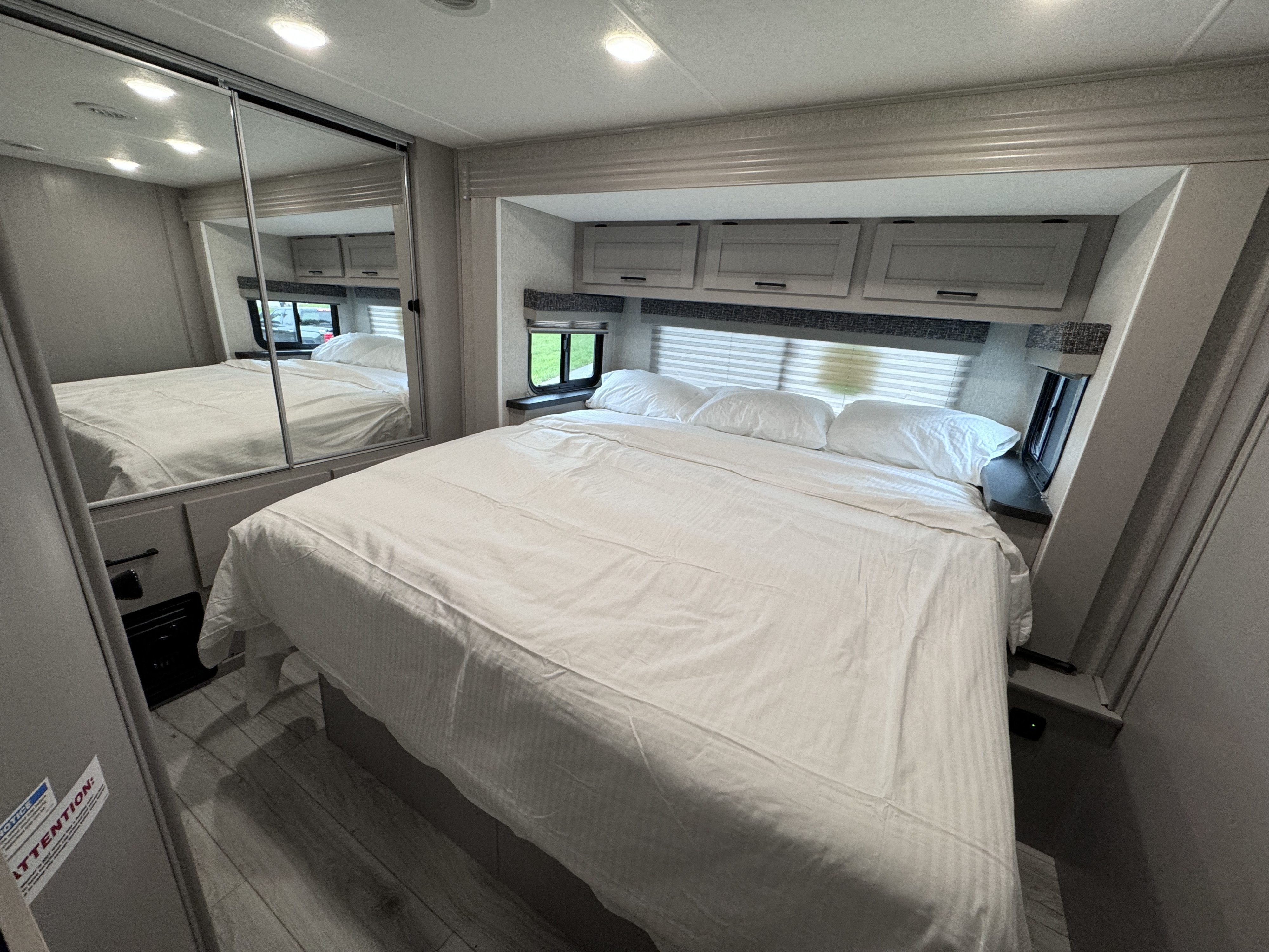 Spacious RV rental bedroom featuring a large bed with fresh white linens, overhead cabinets, and a mirrored closet.. Forest River Coachmen Freelander 2026