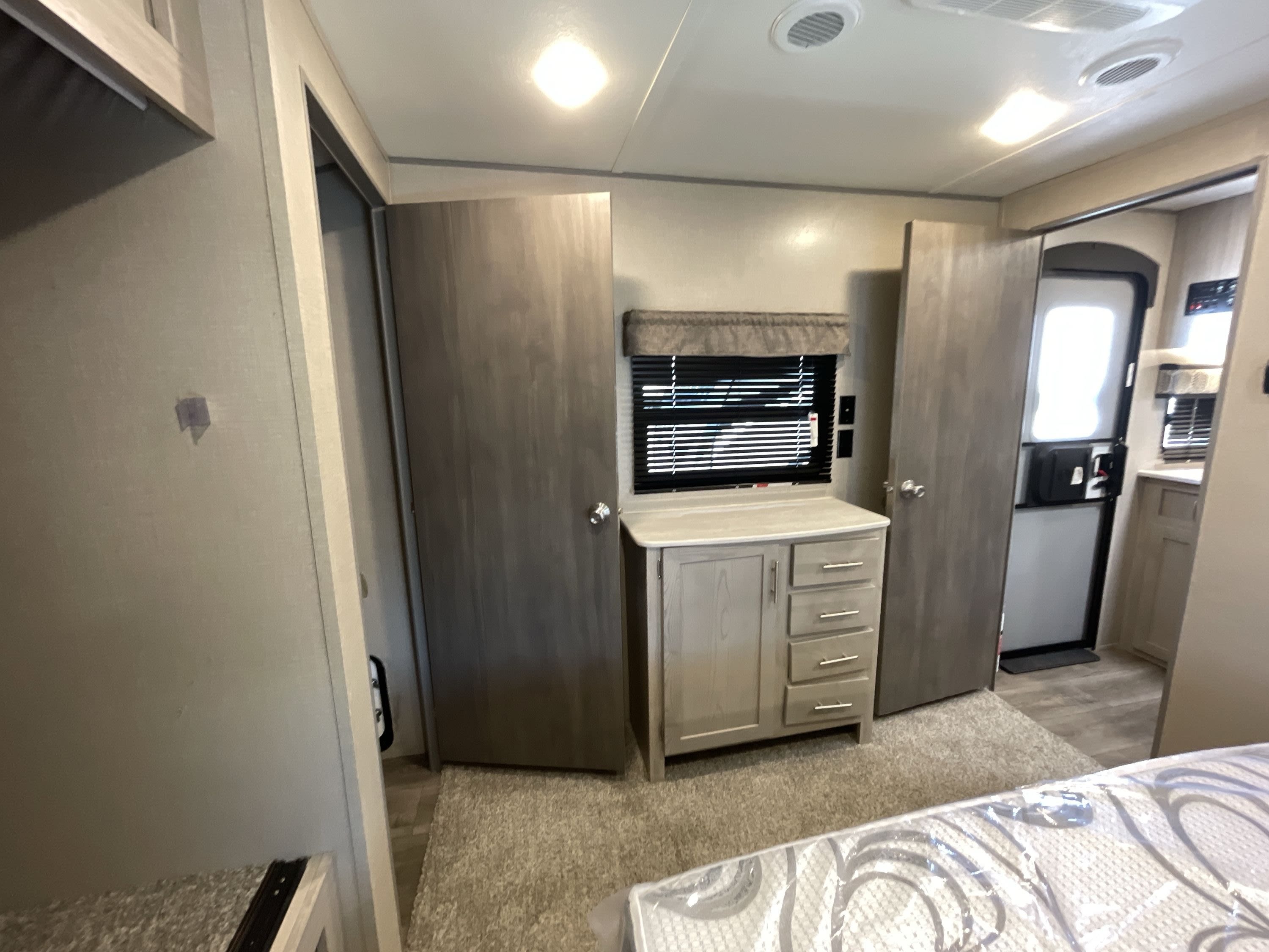 RV rental interior: a neatly arranged bedroom area featuring a new mattress, a dresser with a window, and open interior doors.. Coachmen Catalina 2022