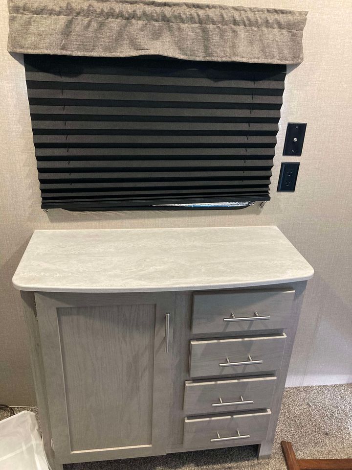 RV rental bedroom interior: window with pleated blinds, functional storage cabinet, and power outlets.. Coachmen Catalina 2022