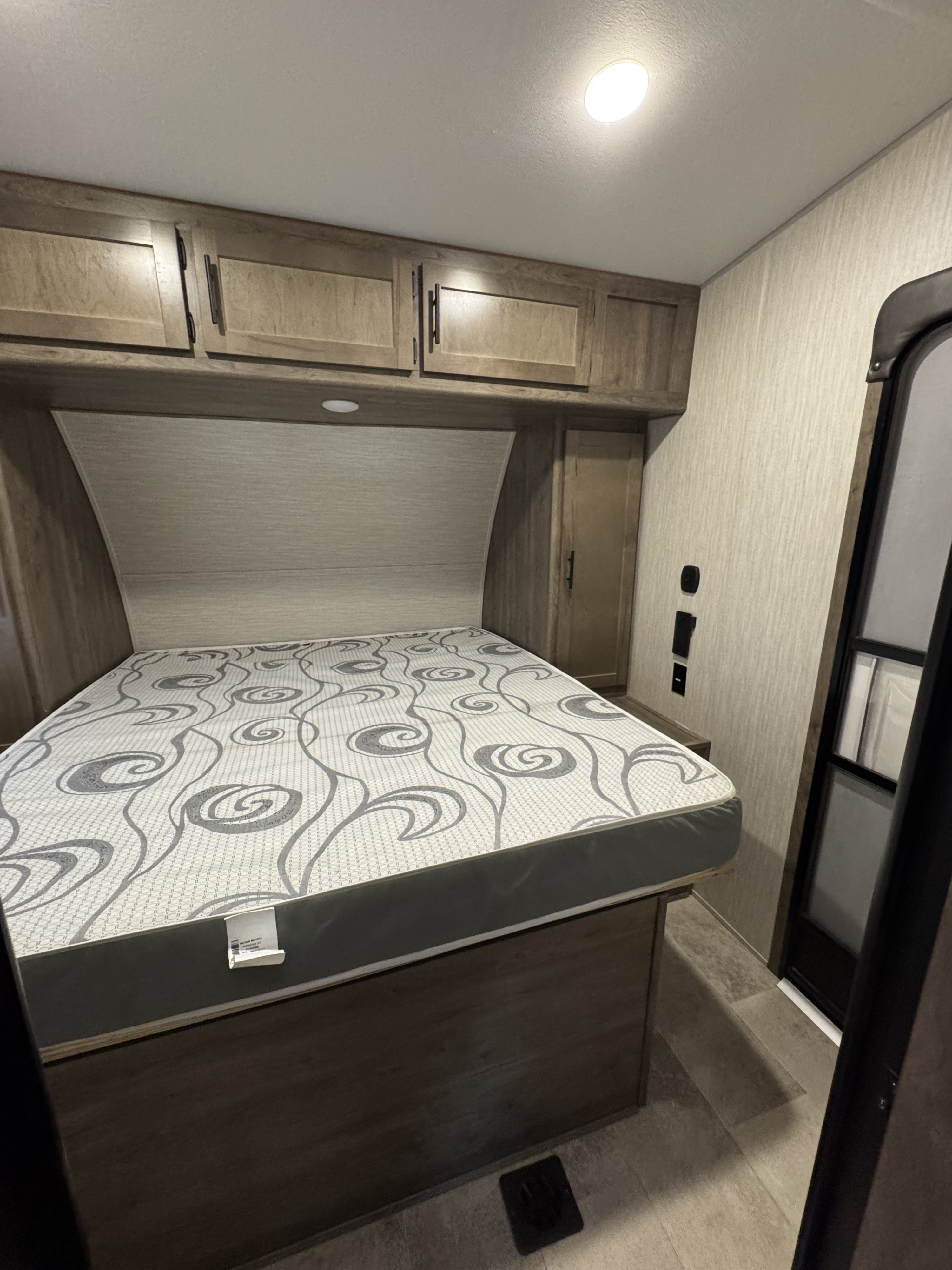 Cozy RV rental bedroom featuring a patterned bed, overhead cabinets, and built-in storage. Perfect for compact travel.. Forest River Vengeance 2020