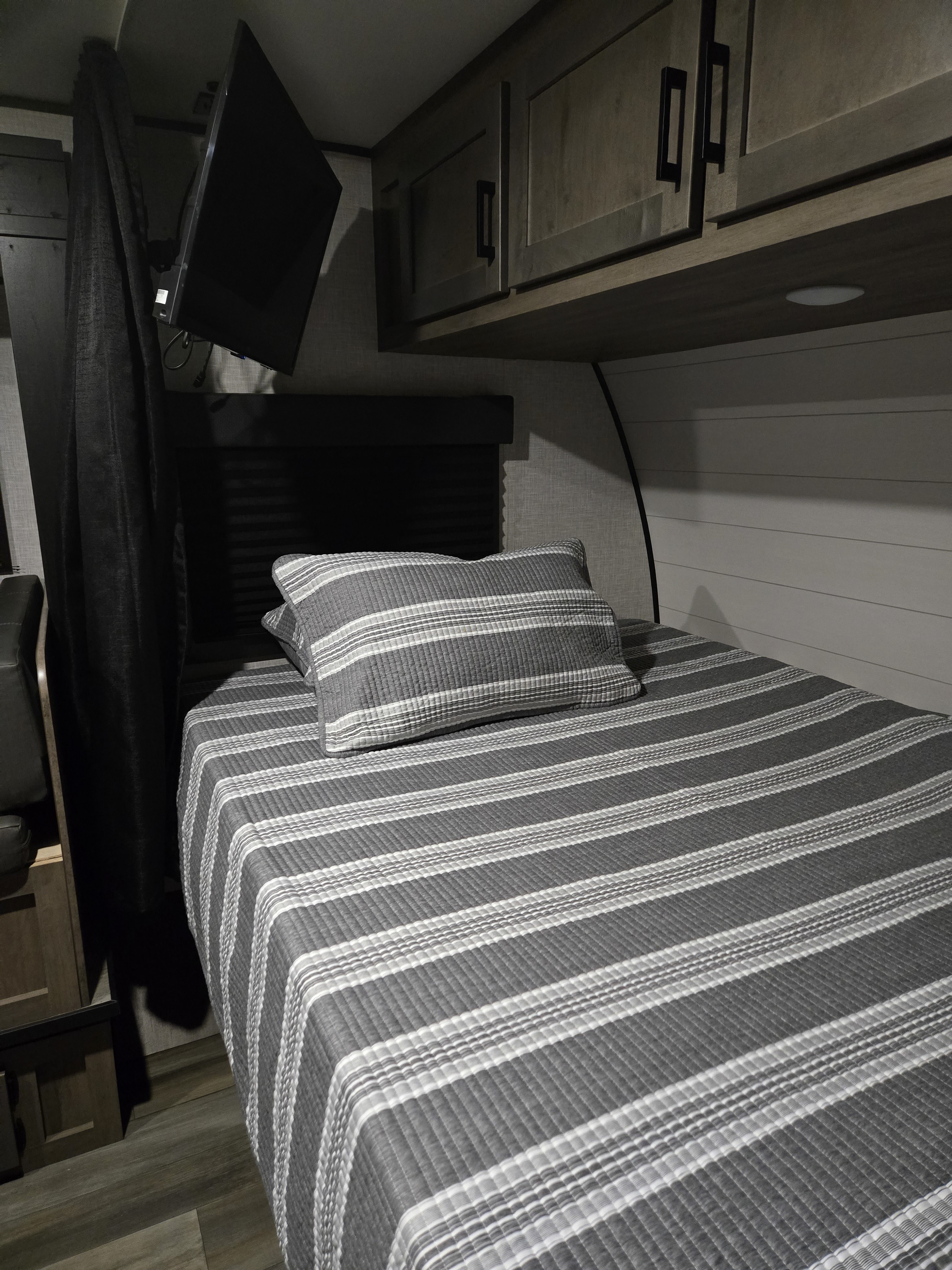 Cozy RV rental bedroom featuring a striped bed, mounted TV, and storage cabinets, ideal for a comfortable stay.. Starcraft Autumn Ridge 2024