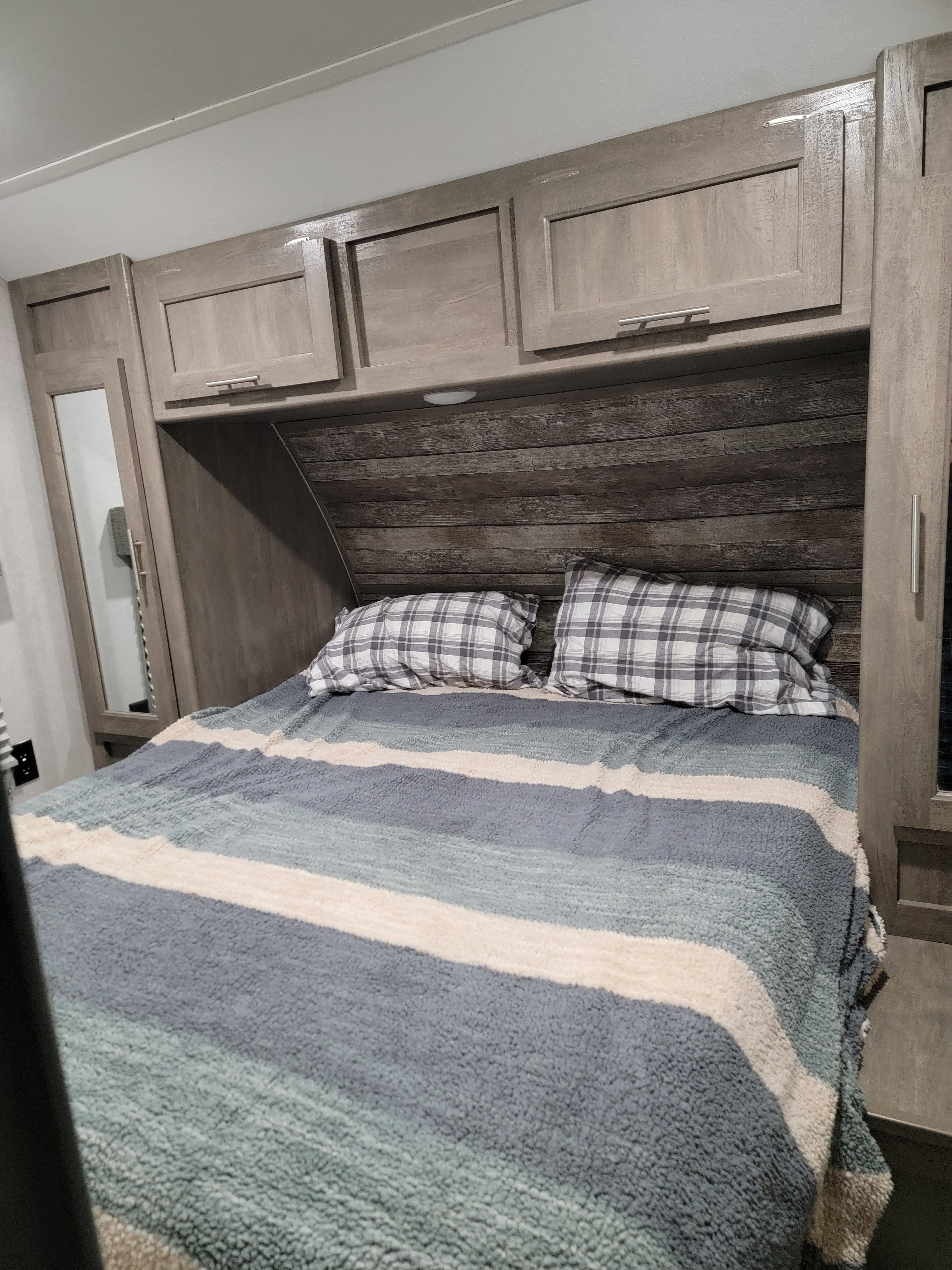 Cozy RV rental bedroom with striped blanket, plaid pillows, wooden cabinets, and a built-in headboard.. XLR BOOST 27QB 2021