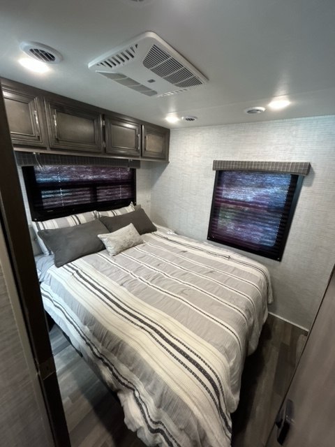 Compact RV rental bedroom with striped bedding, overhead cabinets, and AC unit for comfortable travel.. Entegra Coach Odyssey 2024