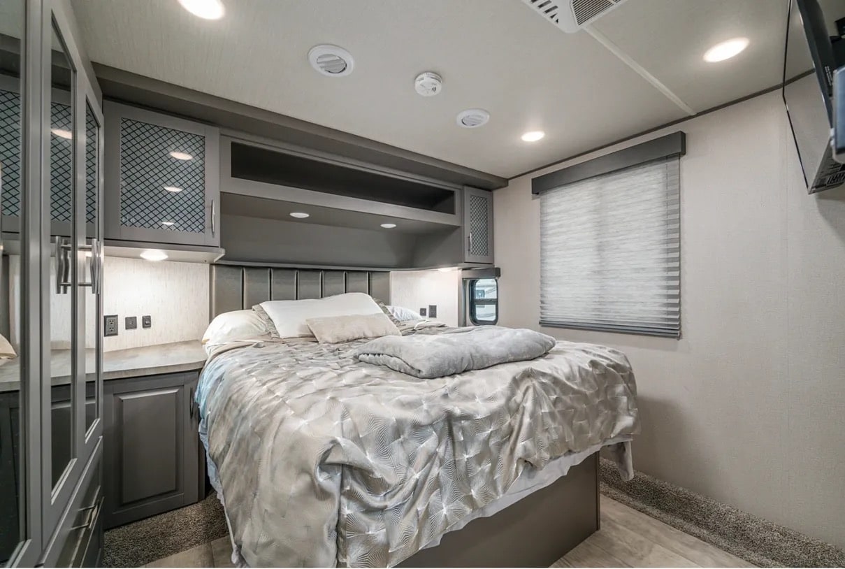 Spacious, modern RV rental bedroom featuring a comfortable bed, overhead storage, ambient lighting, and a large window.. Grand Design Momentum 2021