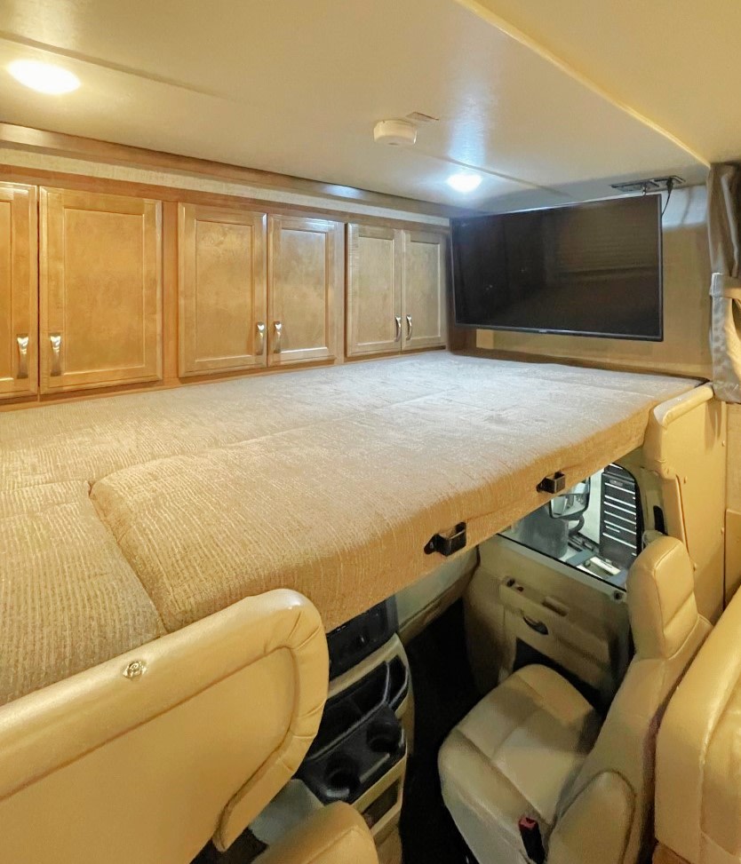 Spacious cab-over bunk bed and storage in an RV rental, with a mounted TV above the driver's cabin.. Gulf Stream Conquest 2020