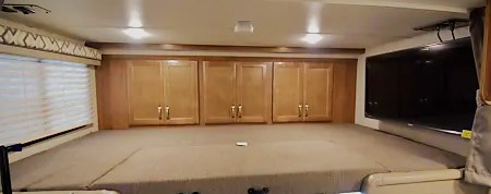 Spacious RV rental cab-over bunk features a bed, ample storage cabinets, a window, and a wall-mounted TV.. Gulf Stream Conquest 2020
