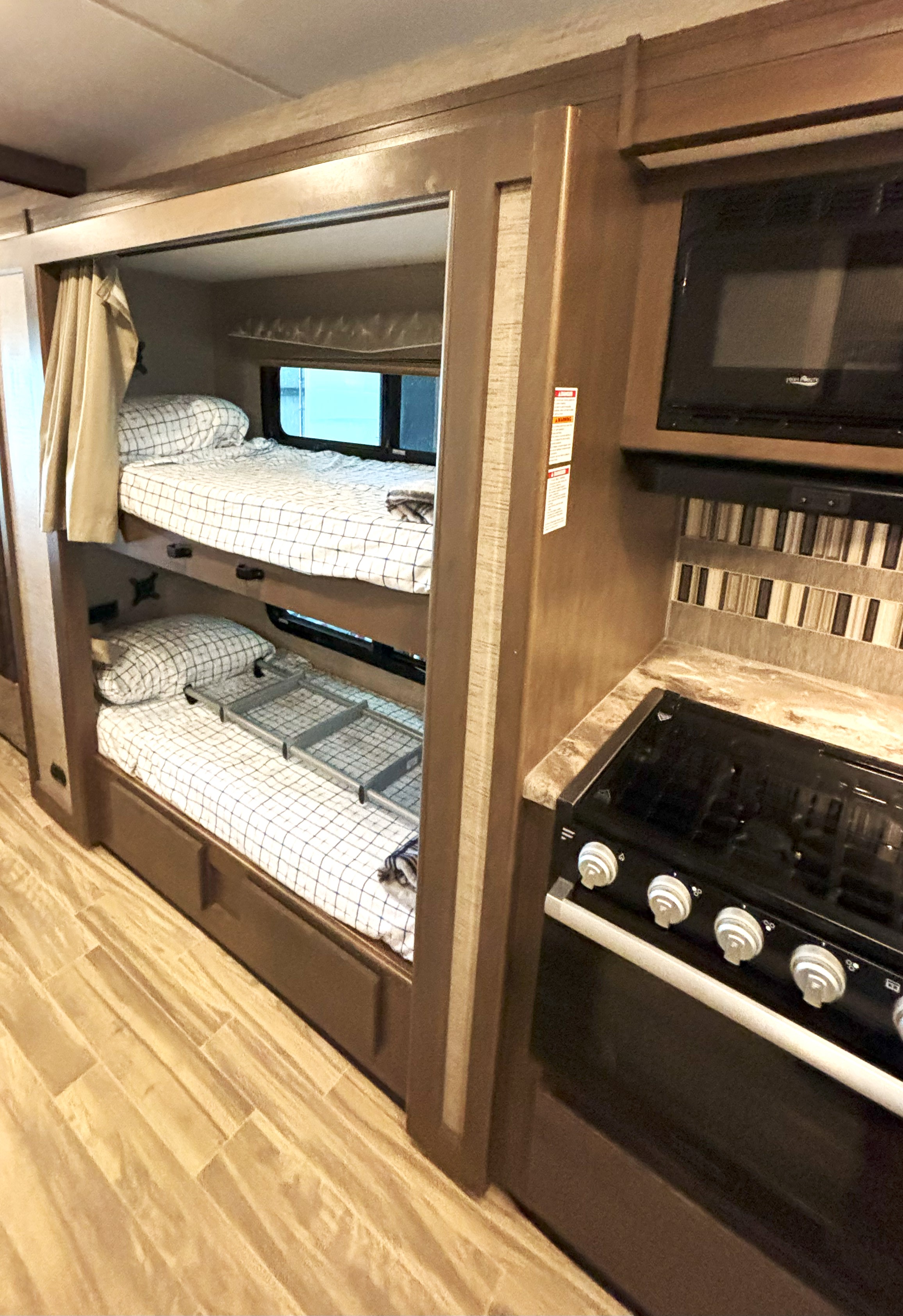RV rental showing cozy bunk beds with checkered sheets, a handy ladder, and a compact kitchen area with stove & microwave.. Thor Motor Coach A.C.E 2022