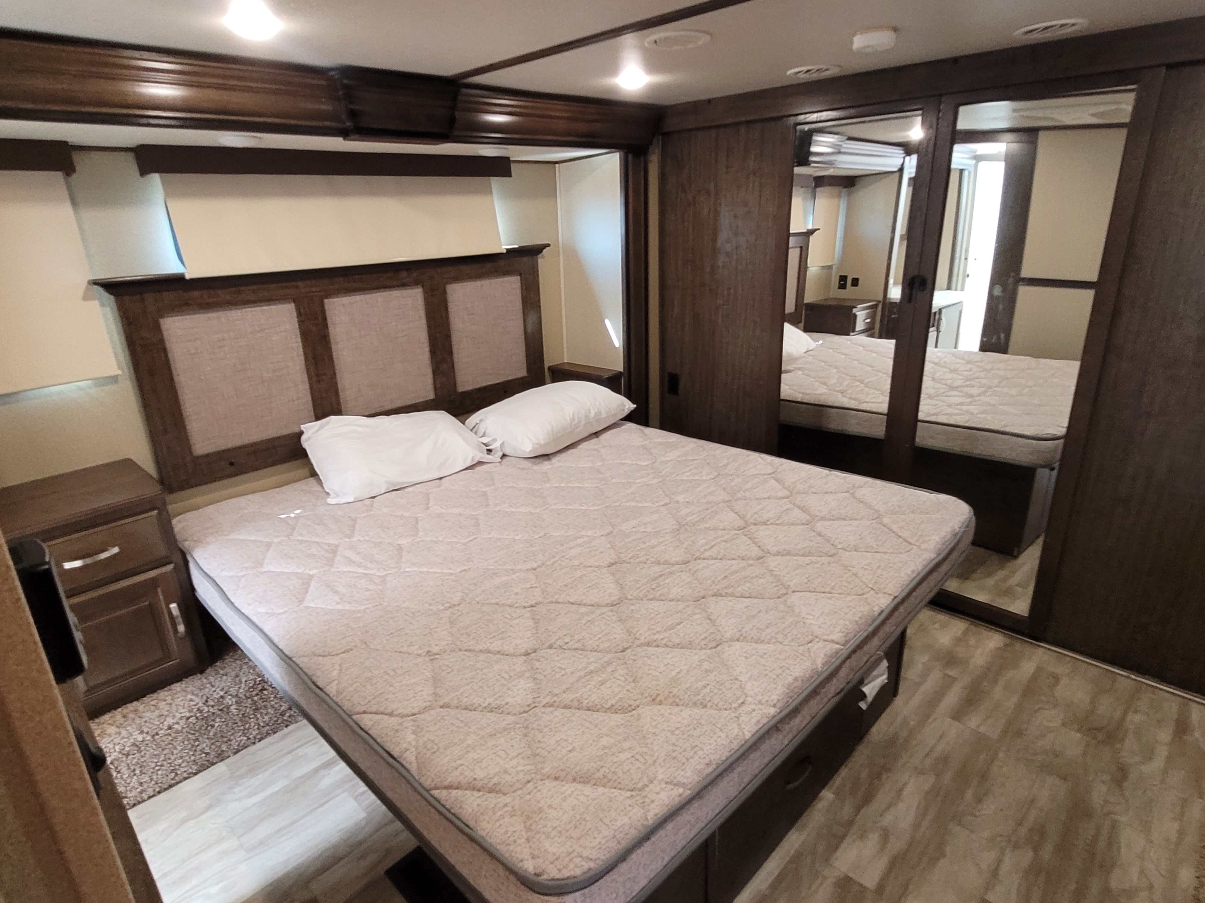 Spacious RV rental bedroom with a large bed, dark wood accents, and mirrored closets, offering a comfortable stay.. Grand Design Solitude 2019