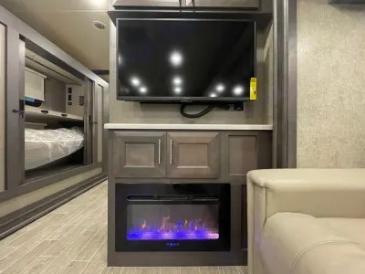 Modern RV rental interior features a wall-mounted TV, electric fireplace with blue flames, and a cozy bunk area.. Thor Miramar 2022