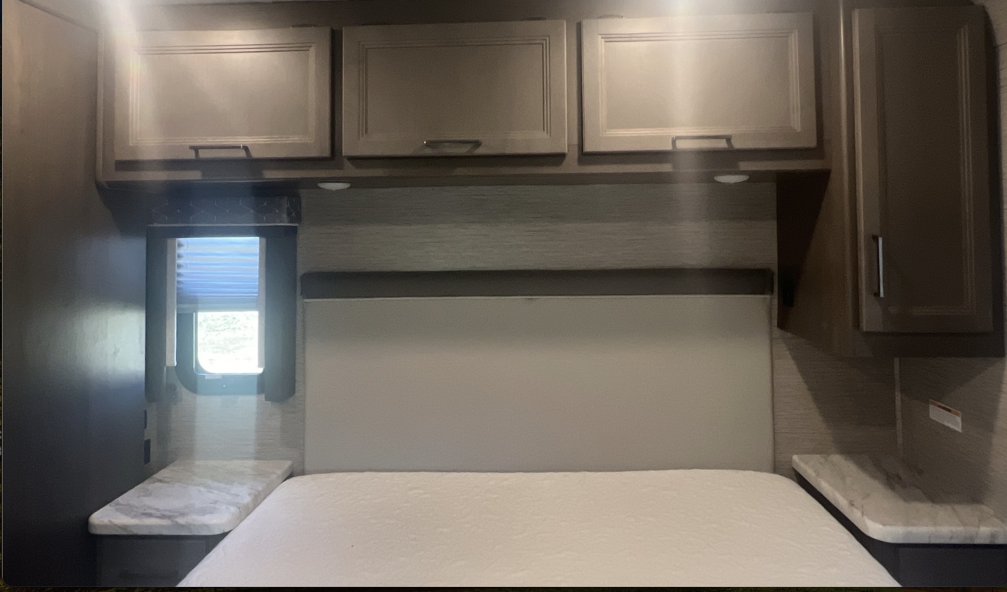 RV rental bedroom interior: compact bed, overhead storage cabinets, side tables, and window with blinds.. Thor Motor Coach Traveler 2023