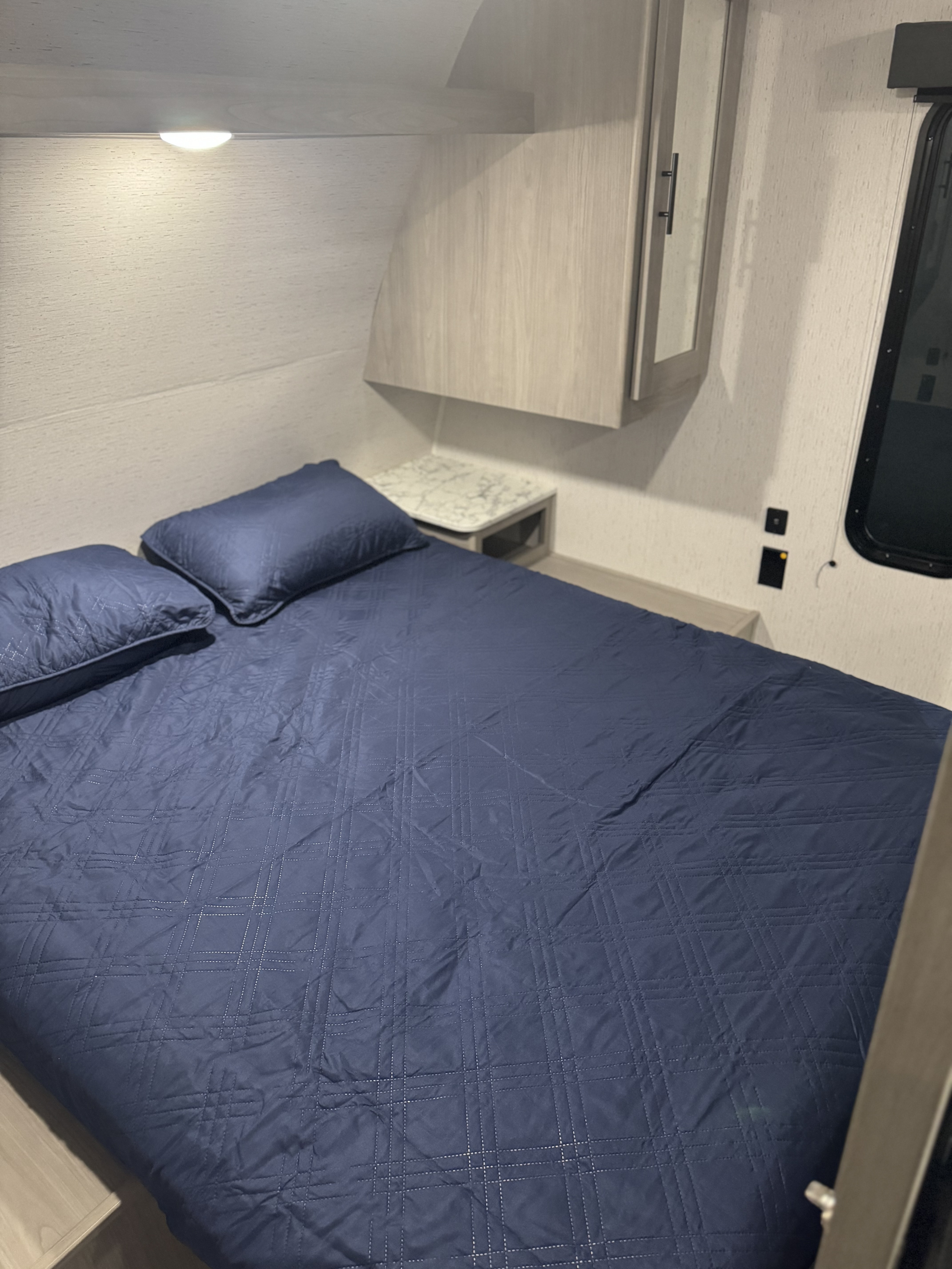 This RV rental bedroom offers a comfortable sleeping space with a quilted blue bed, pillows, and ample storage.. Colman Lantern lt 2024