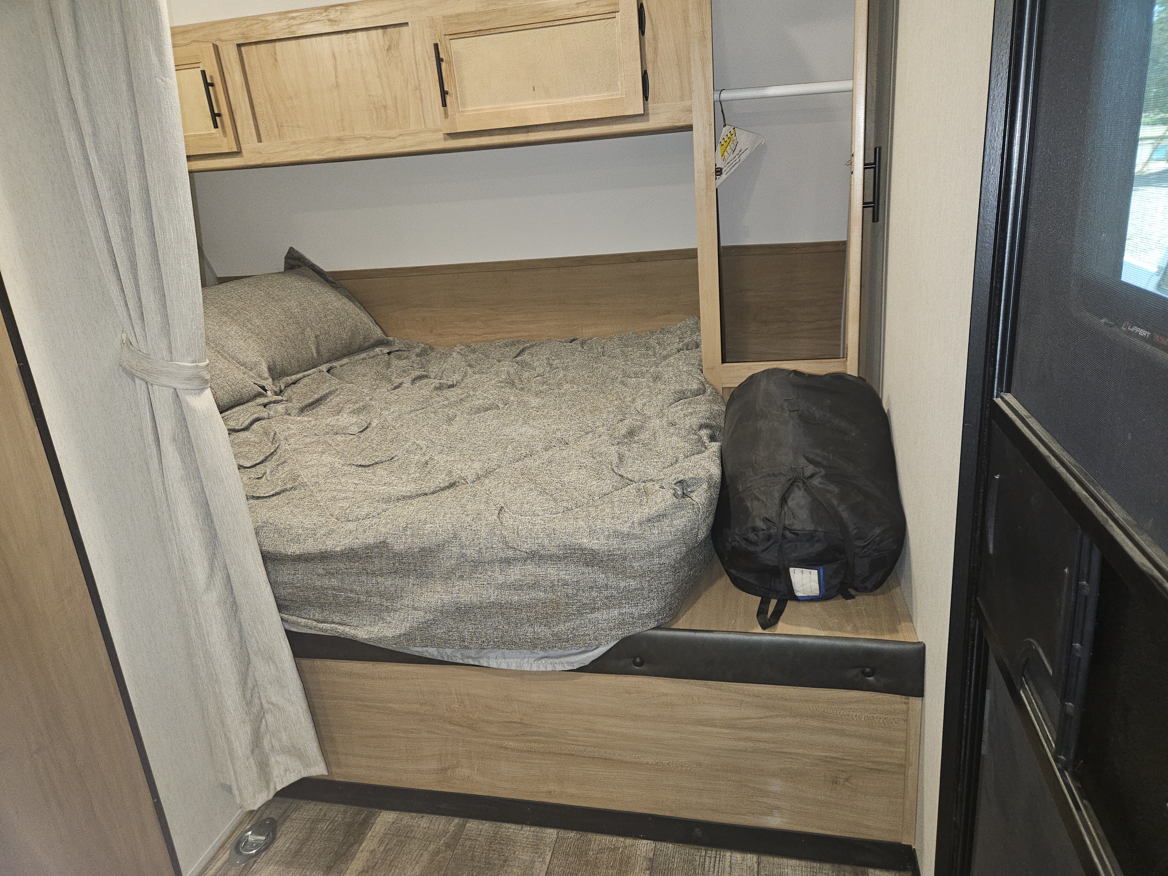 Cozy RV rental bedroom with a gray-textured bed, wooden overhead cabinets, and built-in storage.. Forest River Cherokee 2023