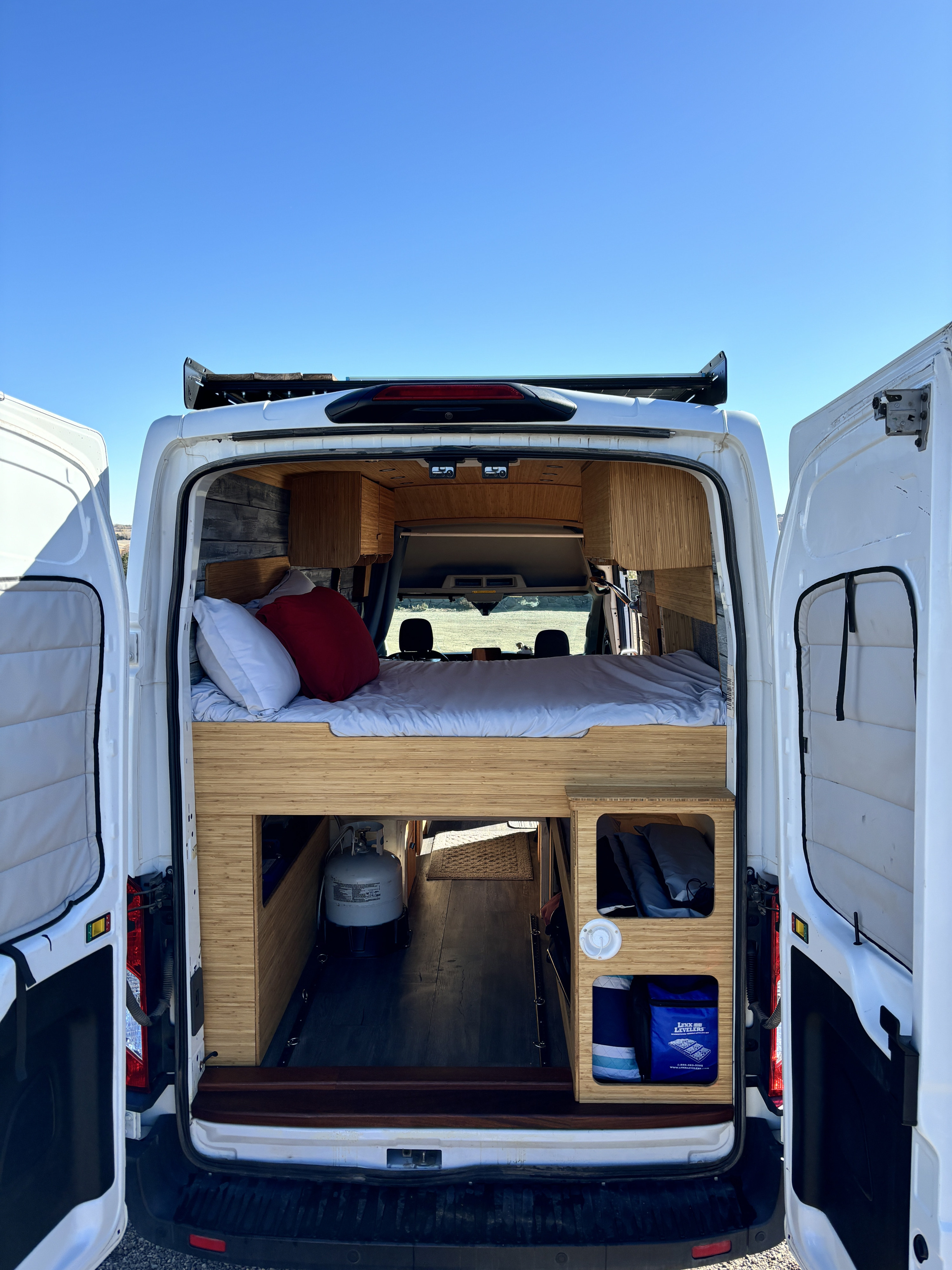 Open doors reveal an RV rental camper van interior: bed, bamboo storage, and propane tank for travel.. Ford Ford Transit 2020
