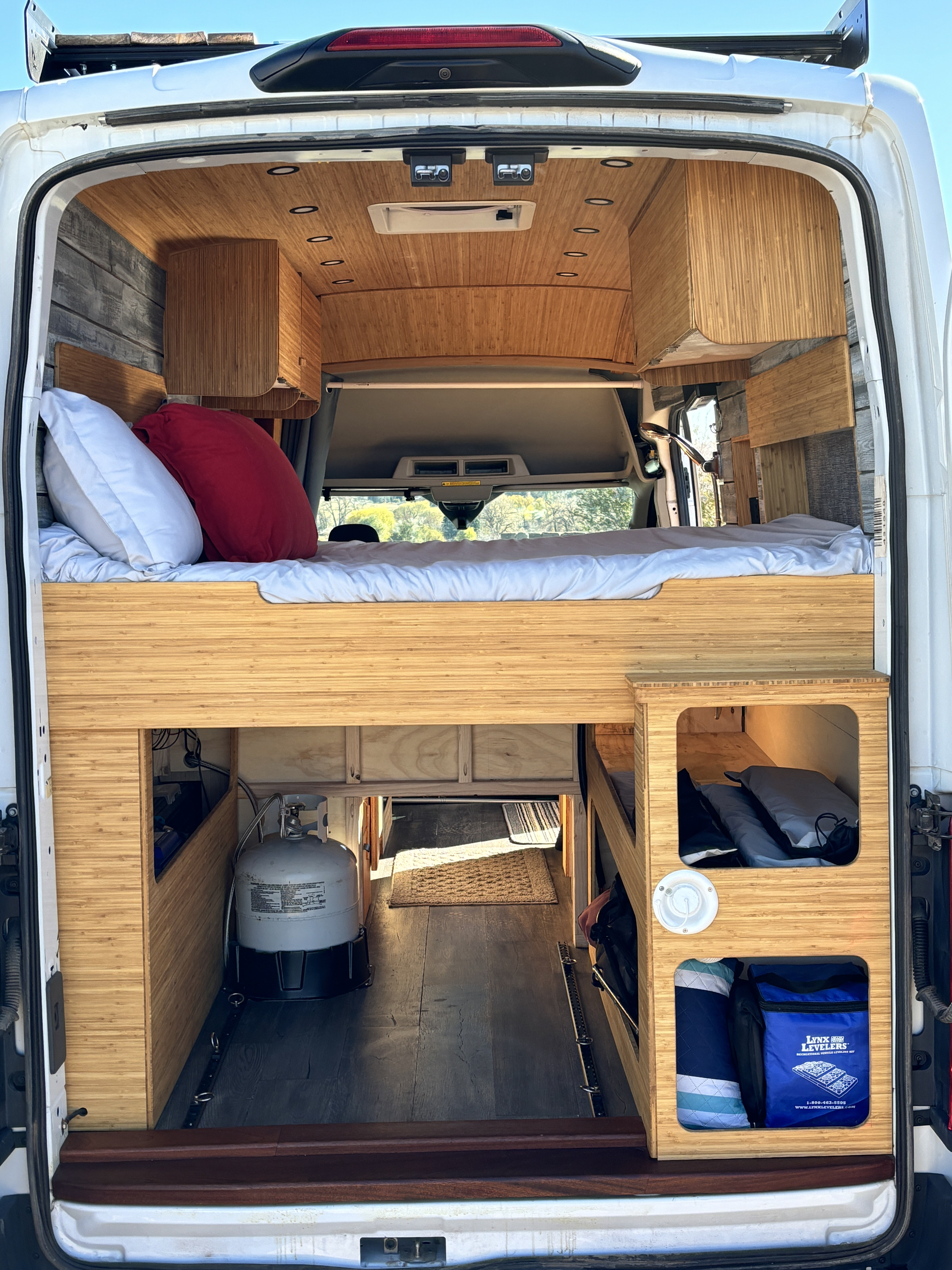 RV rental: Inside a modern camper van, featuring an elevated bed, bamboo wood interior, and functional under-bed storage.. Ford Ford Transit 2020