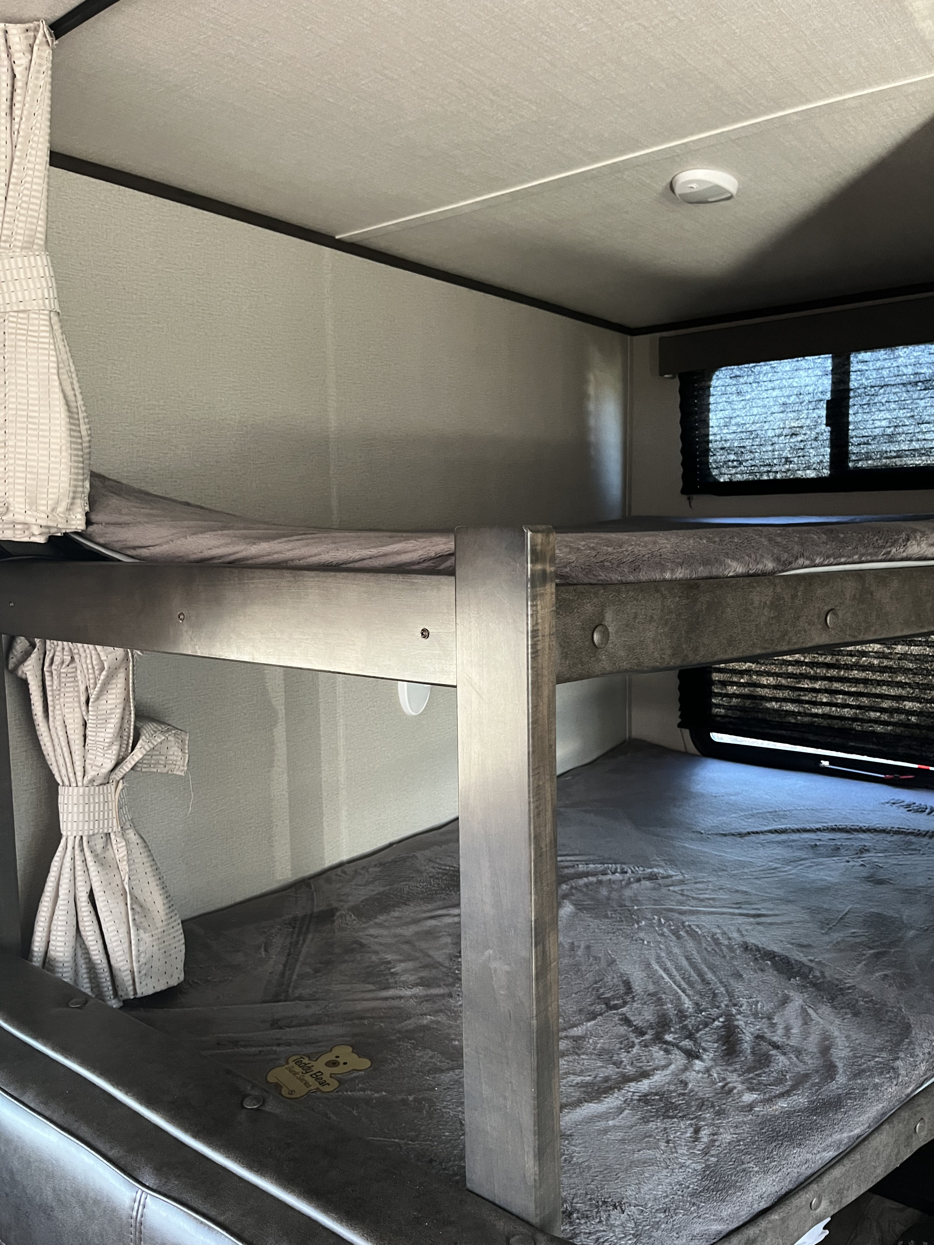 RV rental interior: cozy bunk beds with soft gray blankets, curtains, and a window. Ideal for families.. Grand Design Transcend Xplor 2021