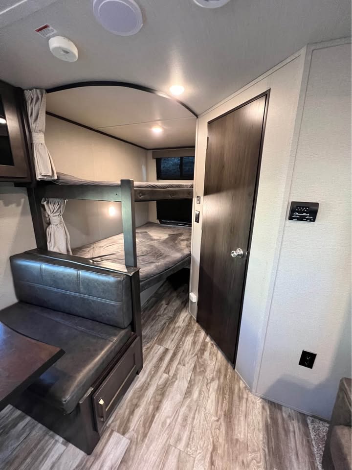 Inside an RV rental: bunk beds with curtains, a dinette with storage, and wood-grain flooring. Cozy and functional.. Grand Design Transcend Xplor 2021