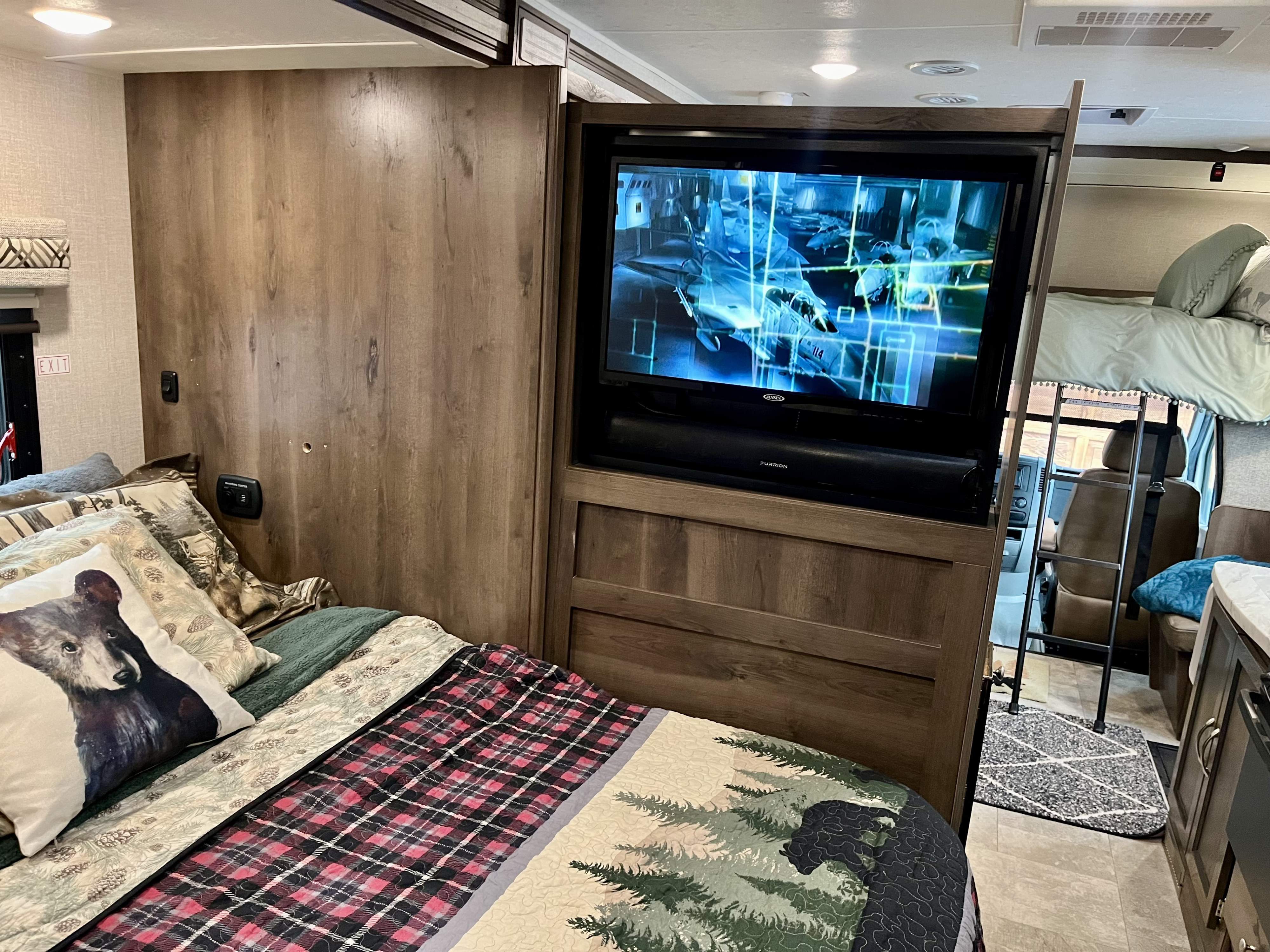 Cozy RV rental interior featuring a bedroom with themed quilts, TV, soundbar, and a bunk bed with ladder.. Coachmen Prism 2019
