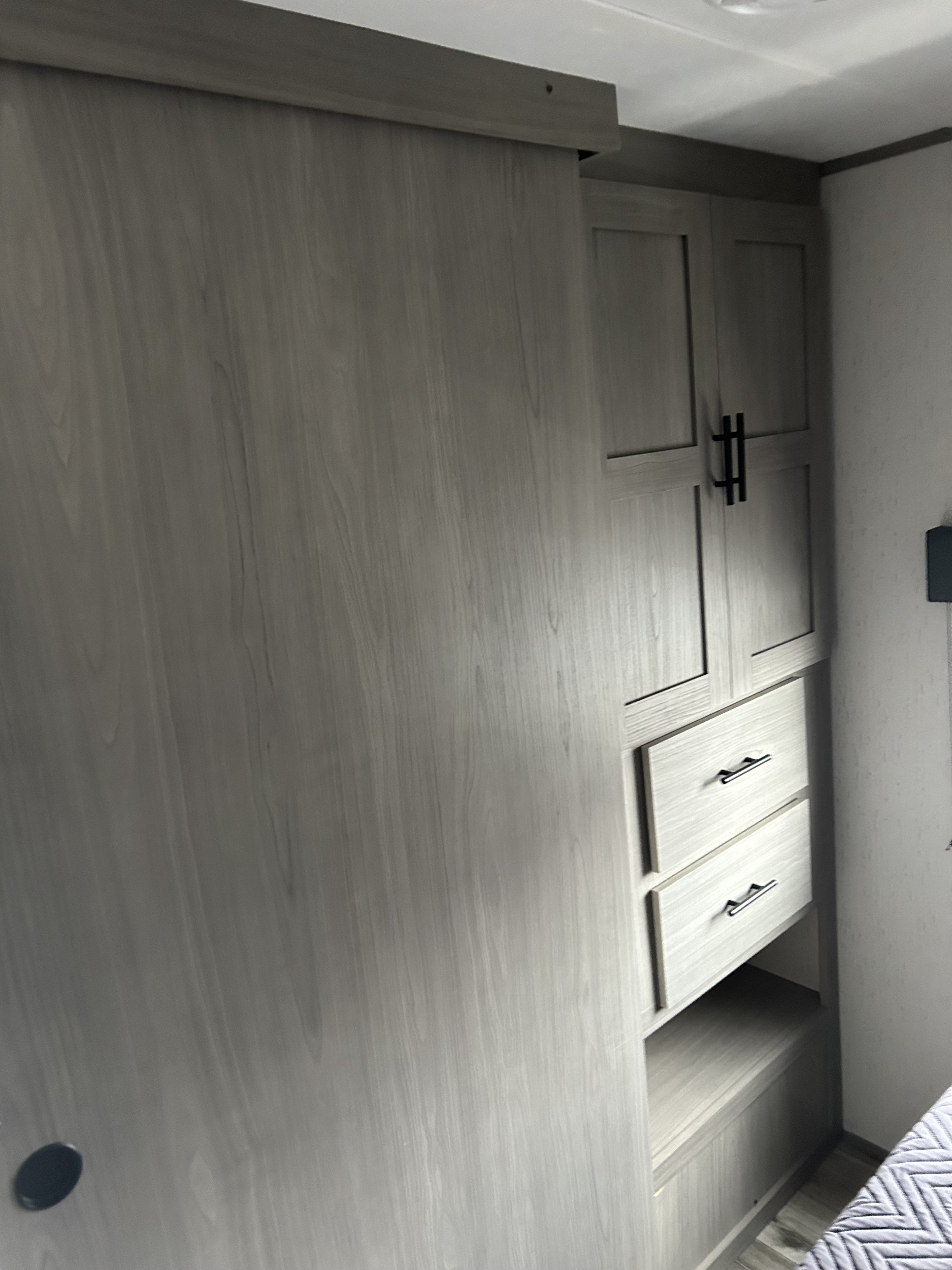 RV rental interior: Light gray wood wardrobe and sliding closet door. Features upper cabinets, drawers, and lower storage by a bed.. Coleman 250tq 2023