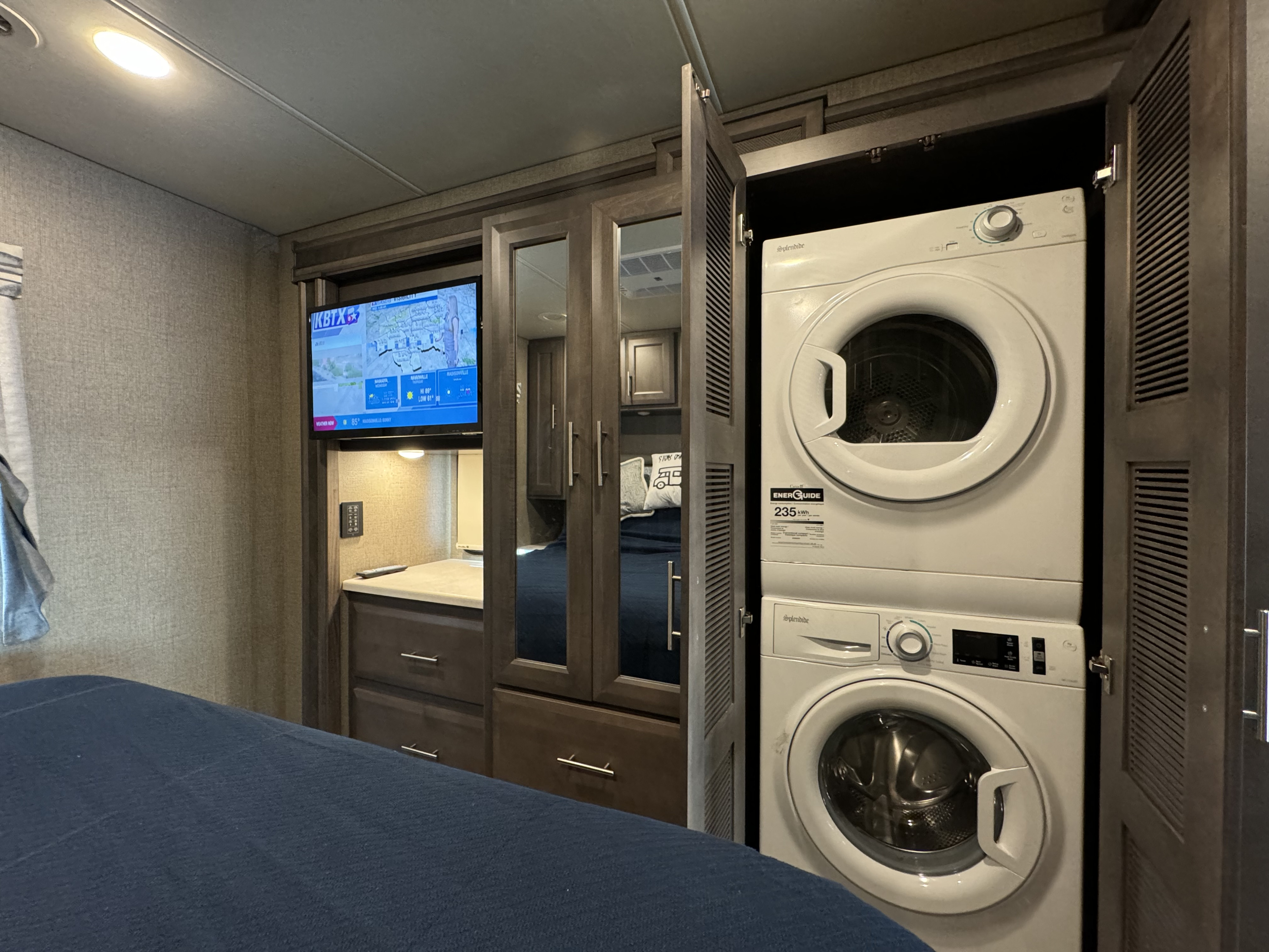 This RV rental bedroom features a TV, ample storage, and a convenient stacked washer/dryer unit.. Thor Motor Coach Miramar 2022