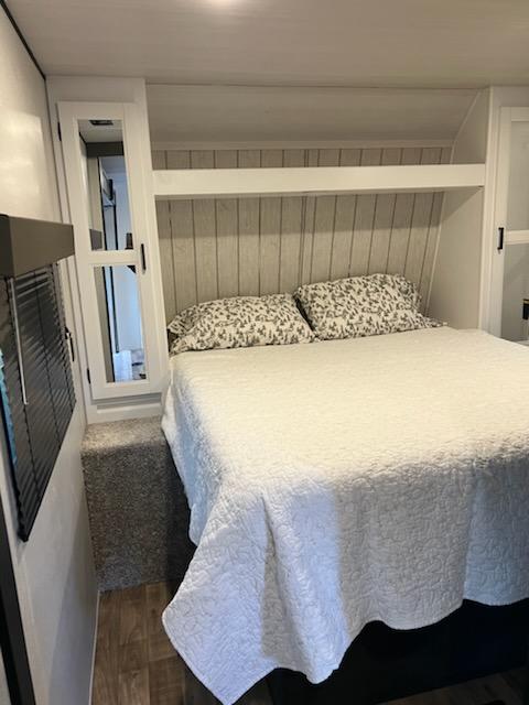 This compact RV rental bedroom features a comfy bed with a white quilt, overhead storage, and a mirrored cabinet.. Keystone RV Hideout 2022