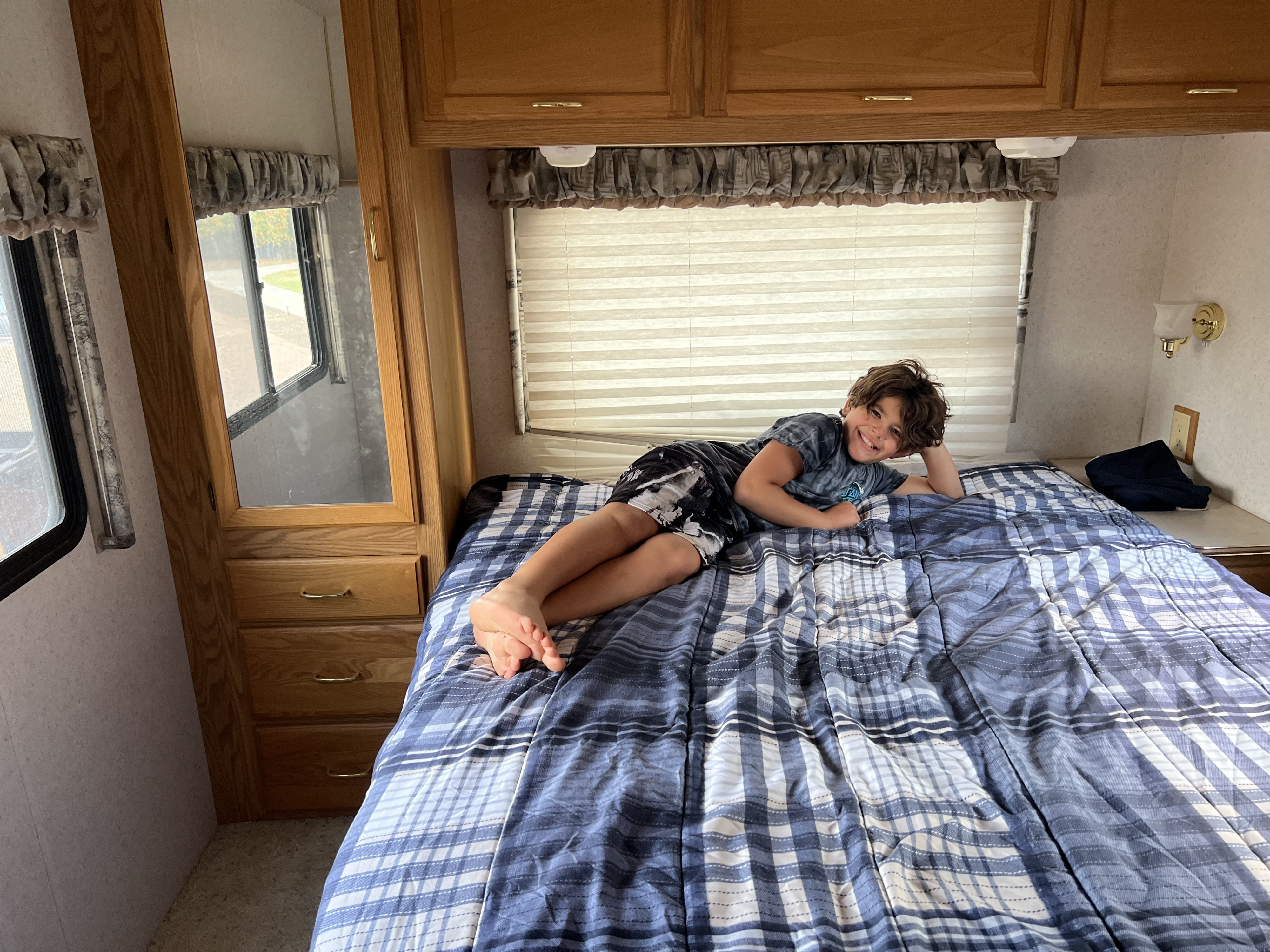 Happy boy relaxing in an RV rental bed, showing the cozy interior with windows and wooden cabinets.. Winnebago Minnie 2002
