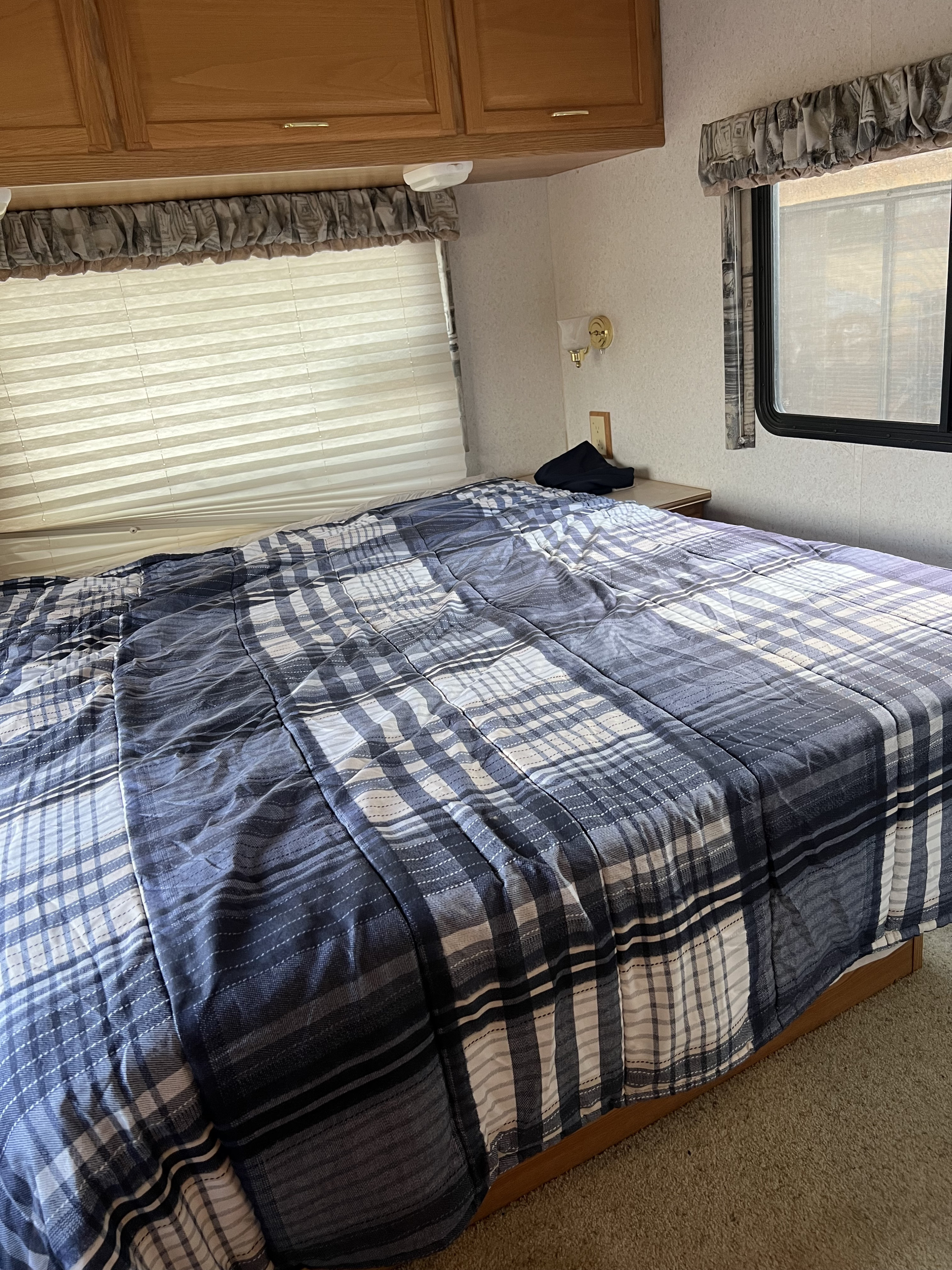Experience comfort in this RV rental bedroom. Features a large bed with plaid comforter, overhead storage, and window blinds.. Winnebago Minnie 2002