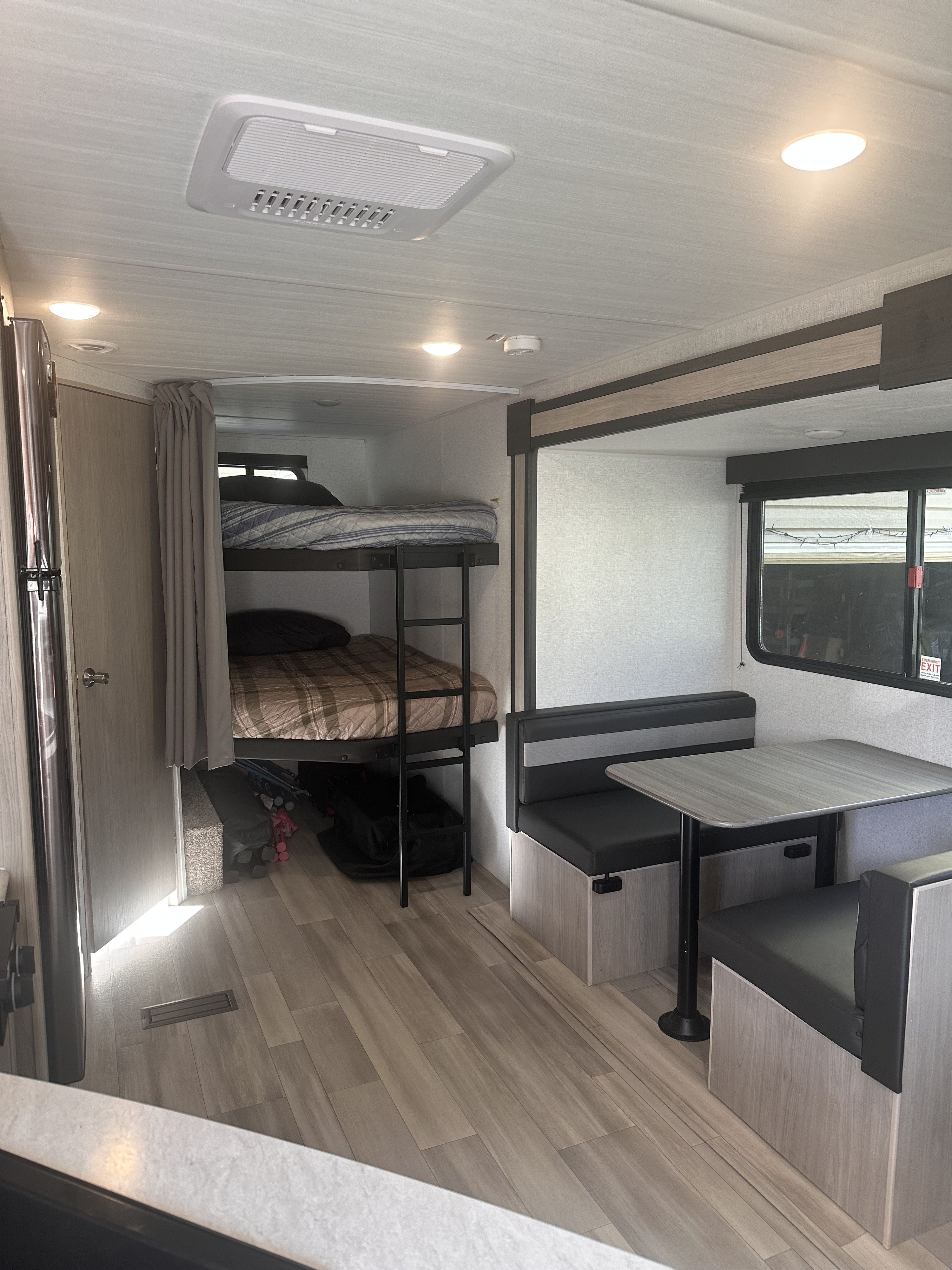 Inside an RV rental: bright interior with bunk beds, a ladder, a cozy dinette, and wood-look flooring.. Keystone RV Springdale 2024