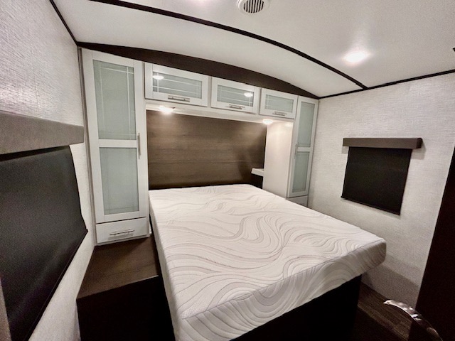 Cozy RV rental bedroom featuring a large bed, overhead cabinets, and a convenient side nightstand for comfortable travel.. Keystone Bullet Premier 2021