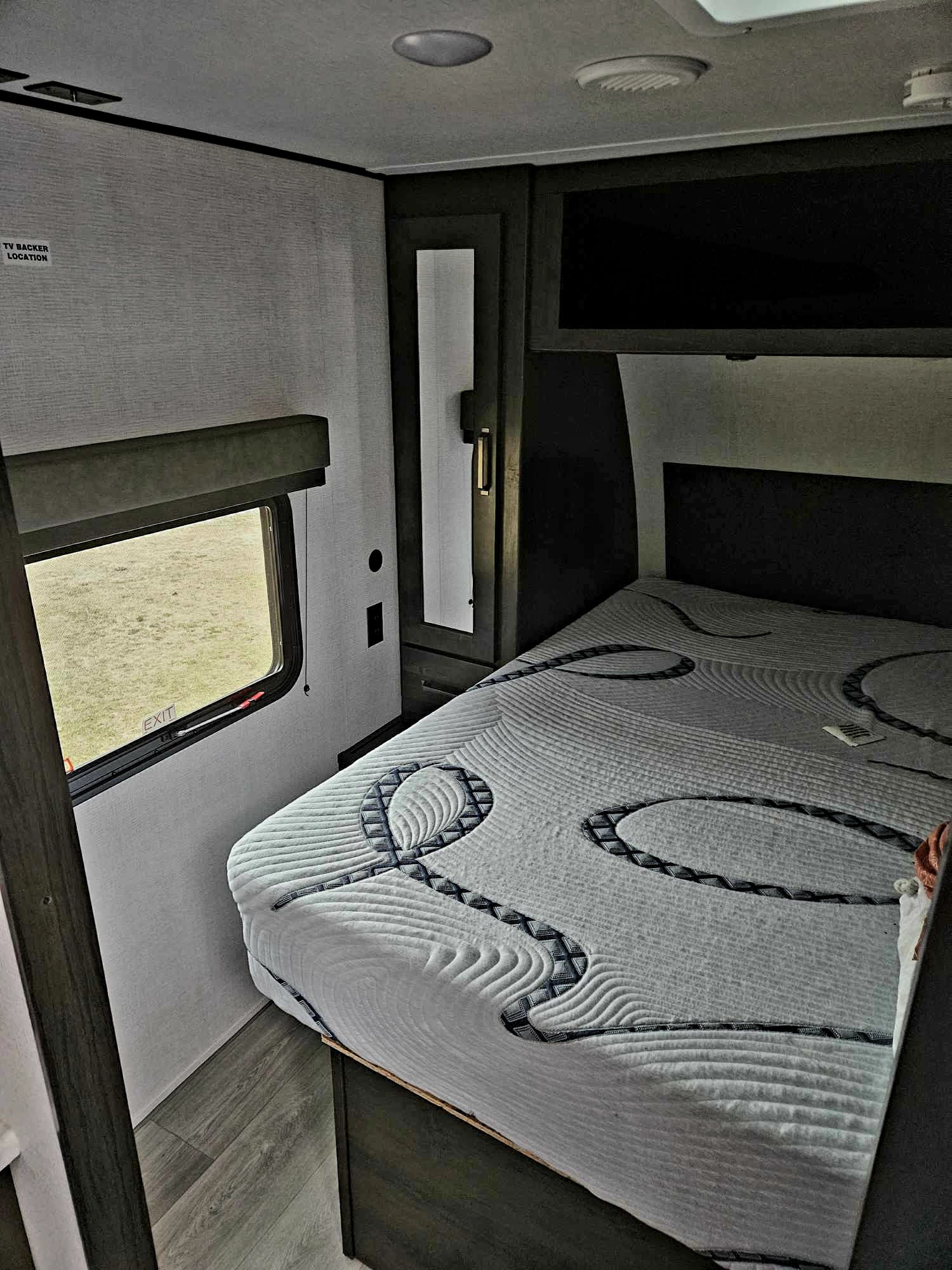 Inside an RV rental bedroom: features a patterned bed, side window, and built-in storage. Compact modern living.. Grand Design Transcend Xplor 2023