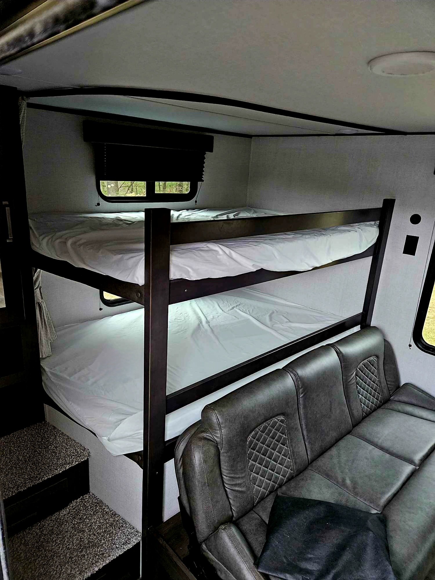 Cozy RV rental interior featuring clean bunk beds and a quilted sofa, perfect for sleeping or lounging.. Grand Design Transcend Xplor 2023