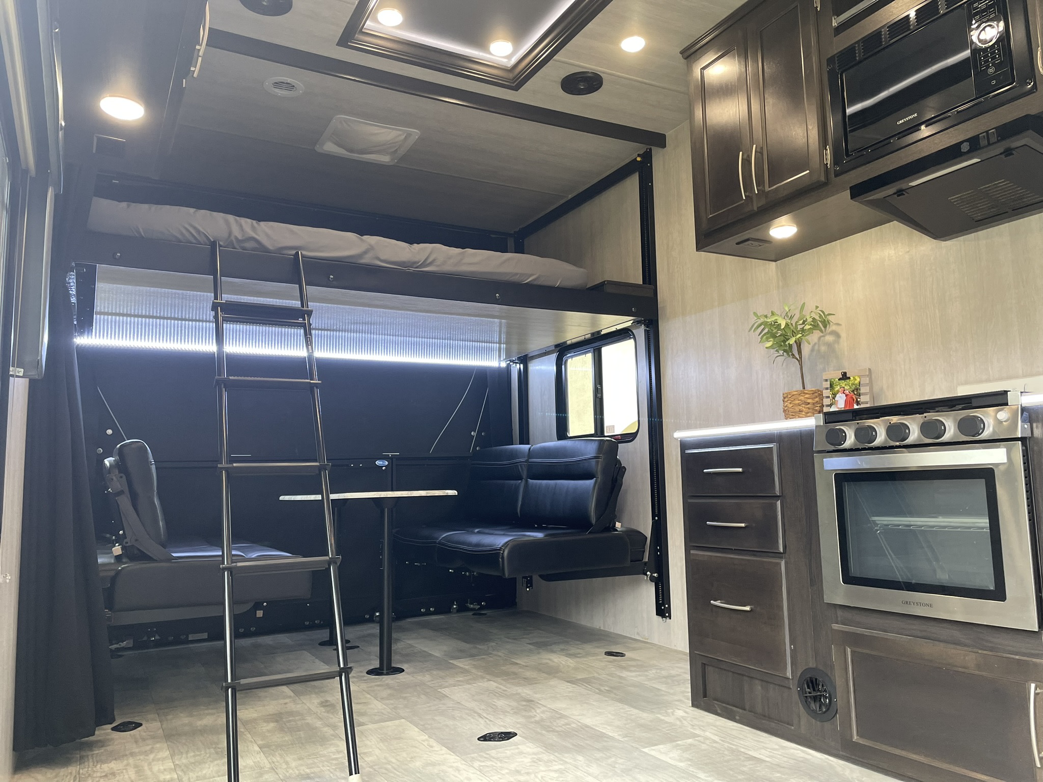 Spacious, modern RV rental interior. Features a full kitchen, overhead bunk bed with ladder, and convertible dinette seating.. Genesis Supreme Sandsport LE Toy Hauler 2022