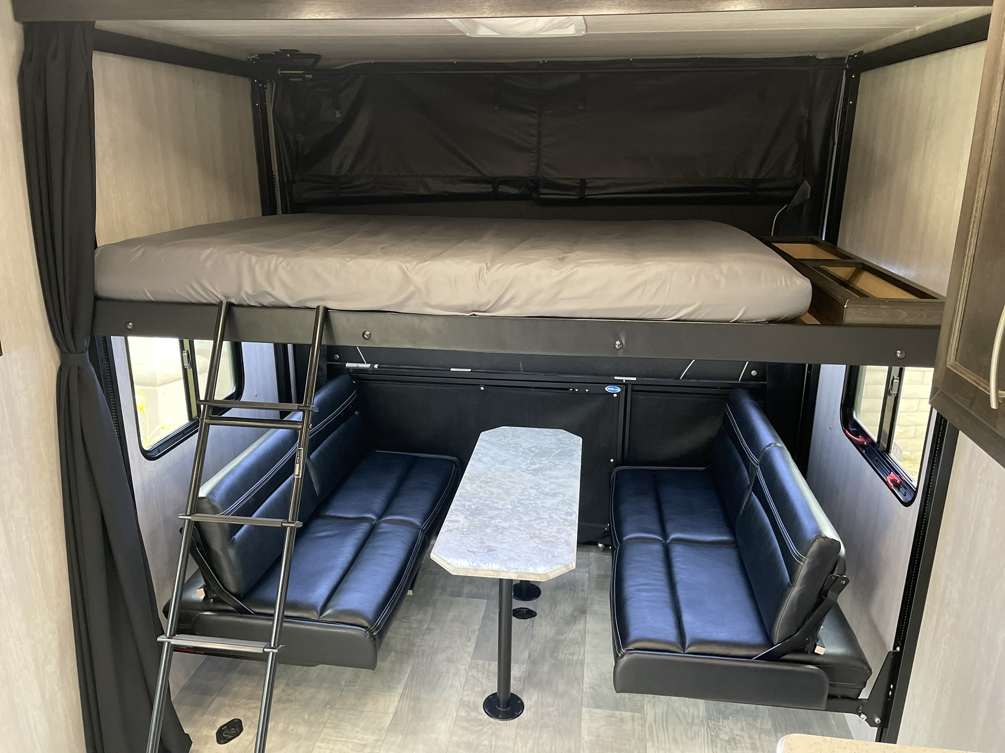 RV rental interior featuring a drop-down bunk bed, ladder, opposing sofas, and a removable table setup.. Genesis Supreme Sandsport LE Toy Hauler 2022