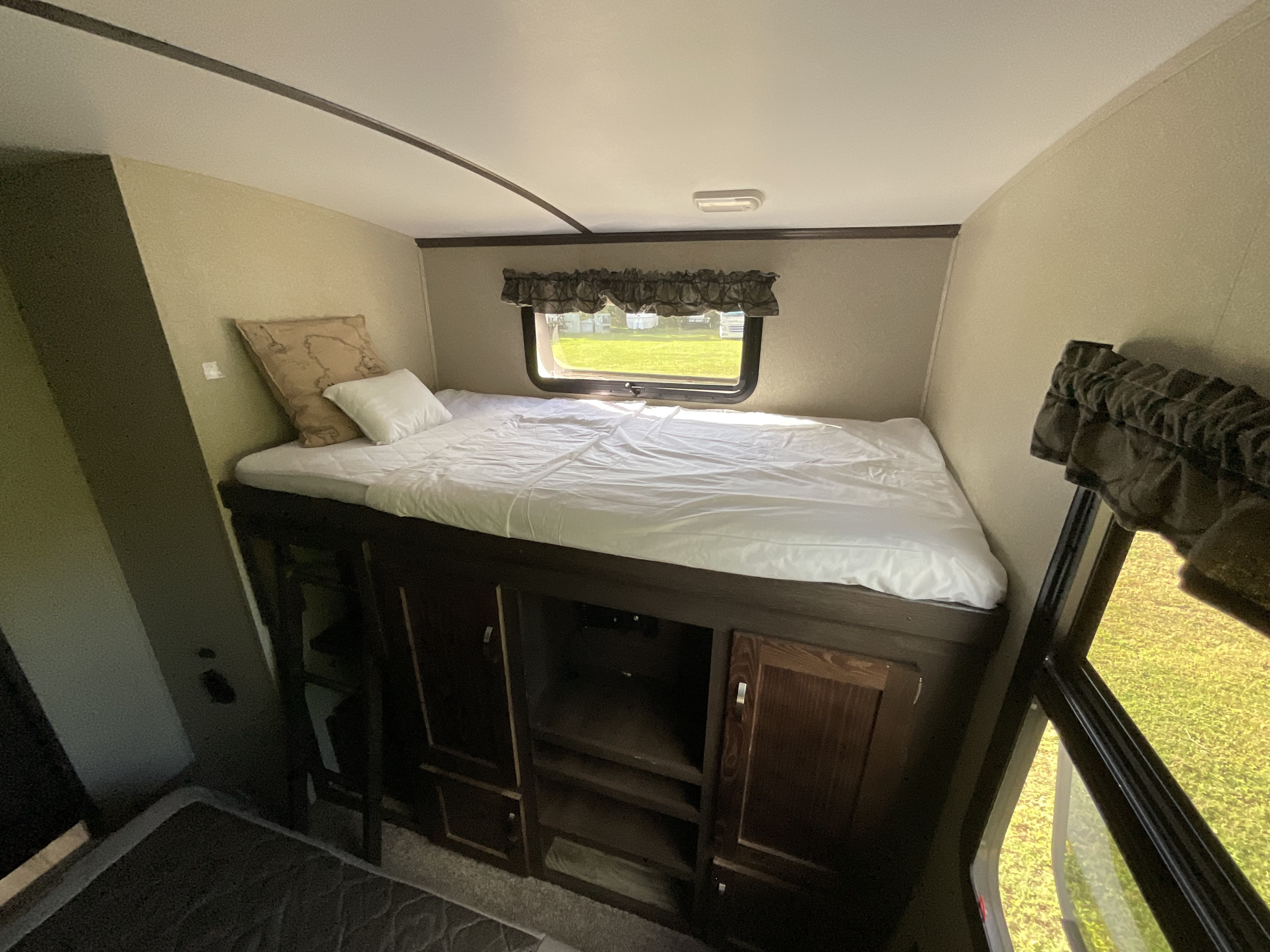 RV rental bunk bed area: elevated bed with white sheets & pillows, built-in storage, and window with outdoor view.. Keystone RV Outback Super-Lite 2018