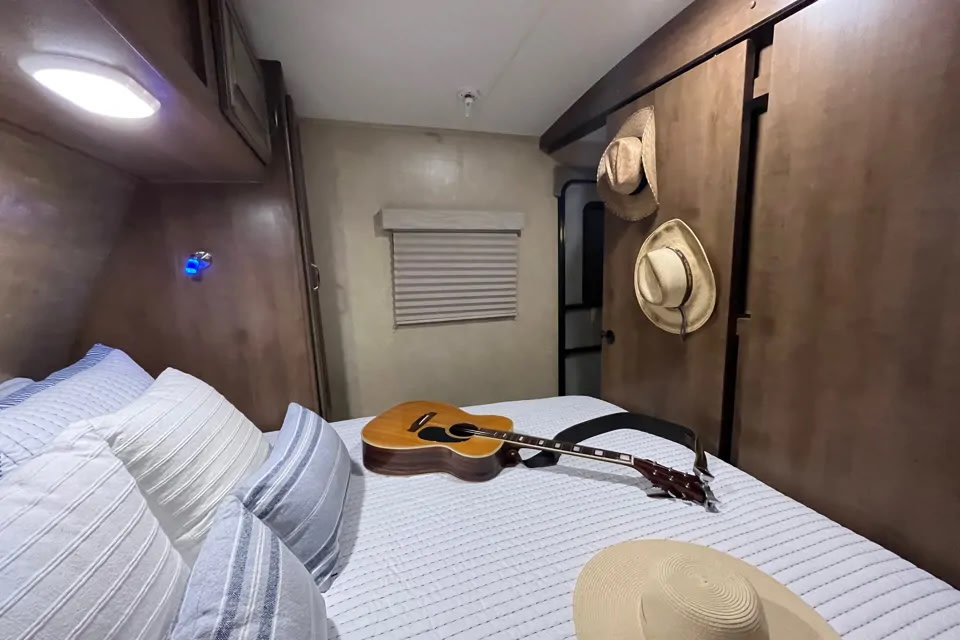 RV rental: a cozy bedroom with striped pillows, an acoustic guitar on the bed, and hats hanging on the wall.. Cruiser RV Fun Finder Xtreme Lite 2016