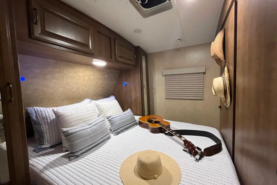 Cozy RV rental bedroom featuring a comfortable bed, guitar, hats, and overhead storage. Ideal for road trip comfort.. Cruiser RV Fun Finder Xtreme Lite 2016