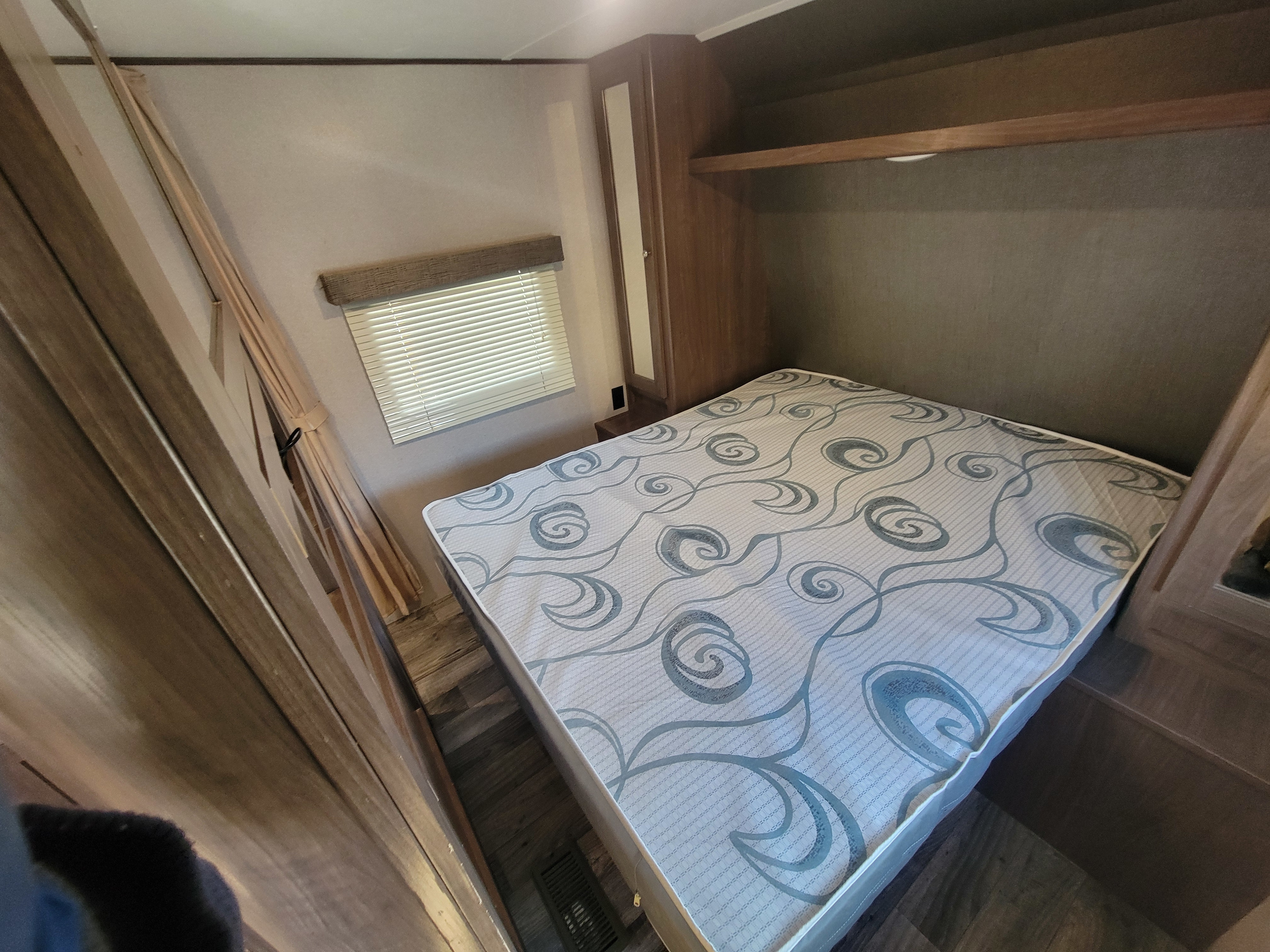 Step inside this RV rental bedroom, featuring a comfy bed with patterned mattress, window, and practical built-in storage.. Keystone RV Hideout LHS 2019