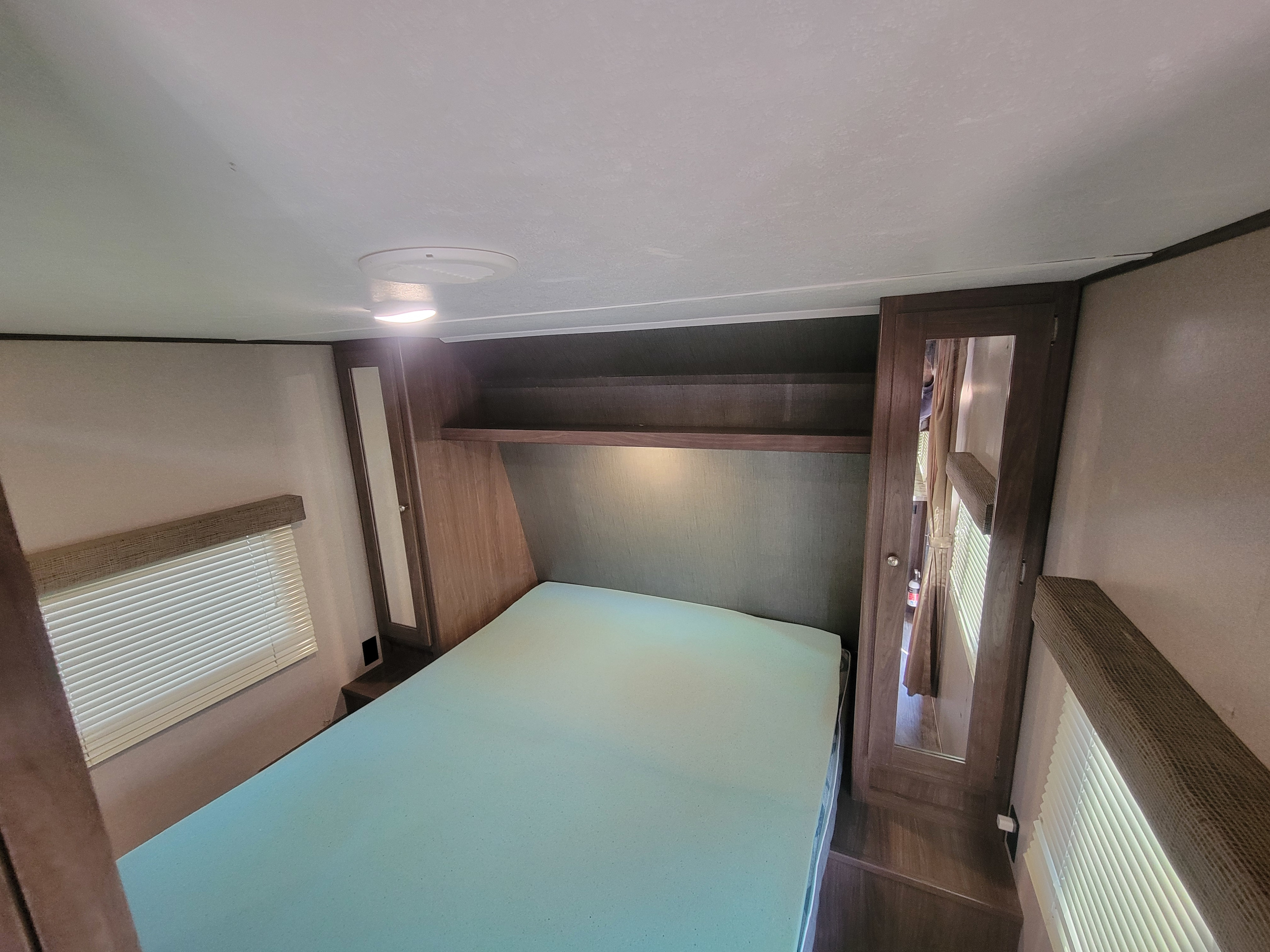Cozy RV rental bedroom featuring a foam bed, overhead shelf, mirrored wardrobe, and window blinds.. Keystone RV Hideout LHS 2019