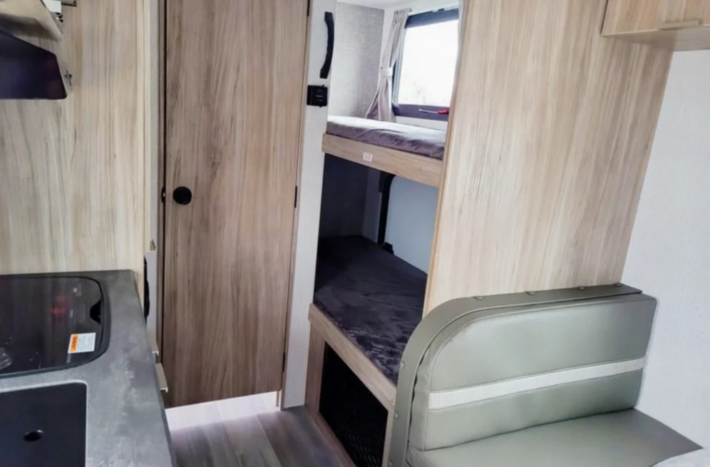 Inside an RV rental: light wood interior with bunk beds, compact kitchen, and dinette. Ideal for family adventures.. Winnebago Minnie Winnie 2022